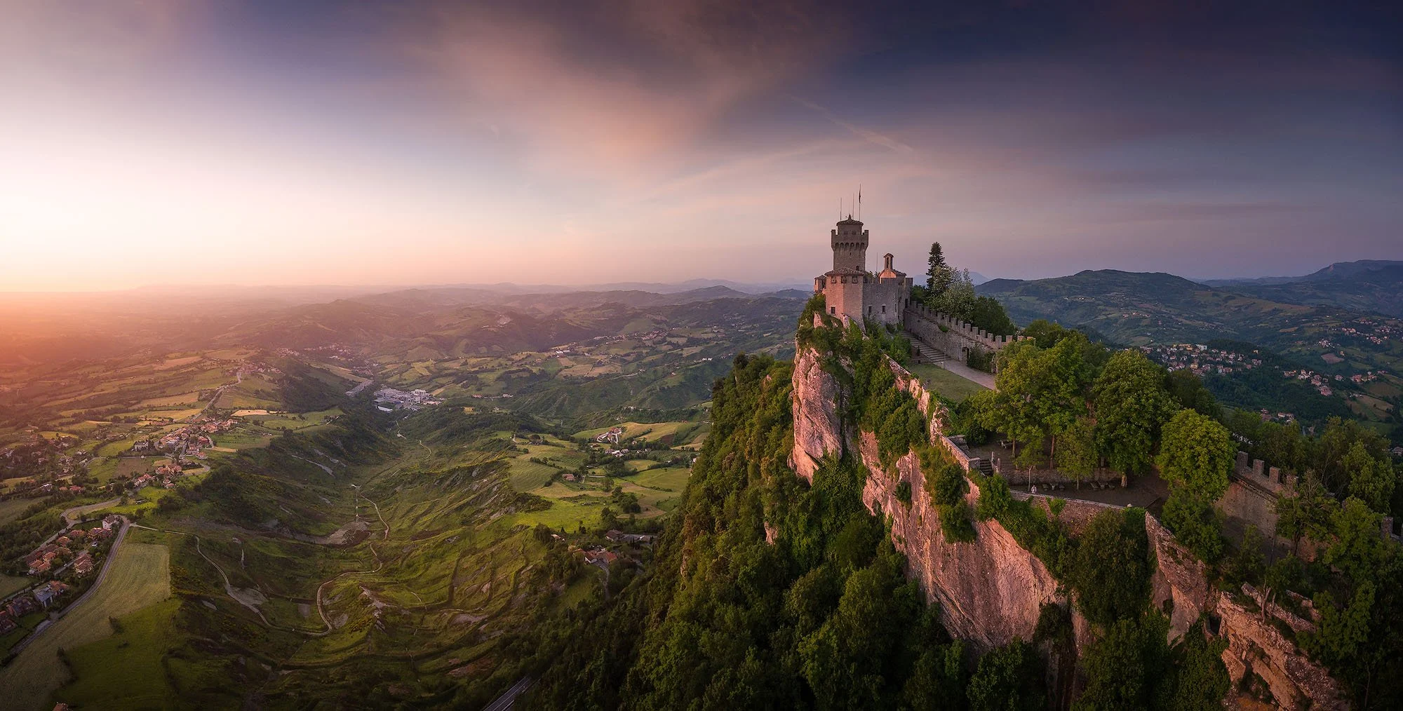 A castle perched on a cliff overlooking a valley during sunset in daytime.