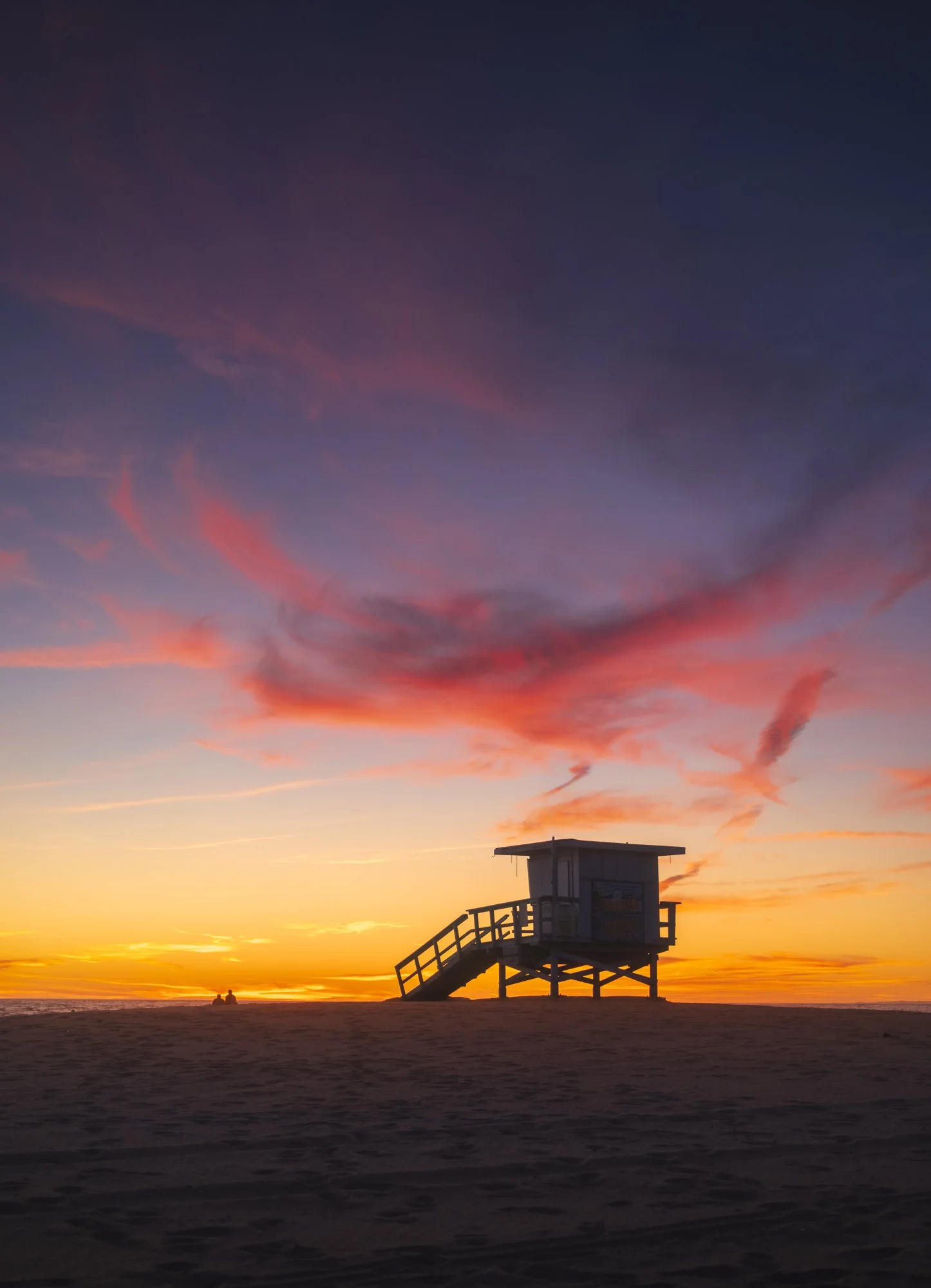 A lifeguard tower on the beach at sunset, with a colorful sky of pink and purple clouds