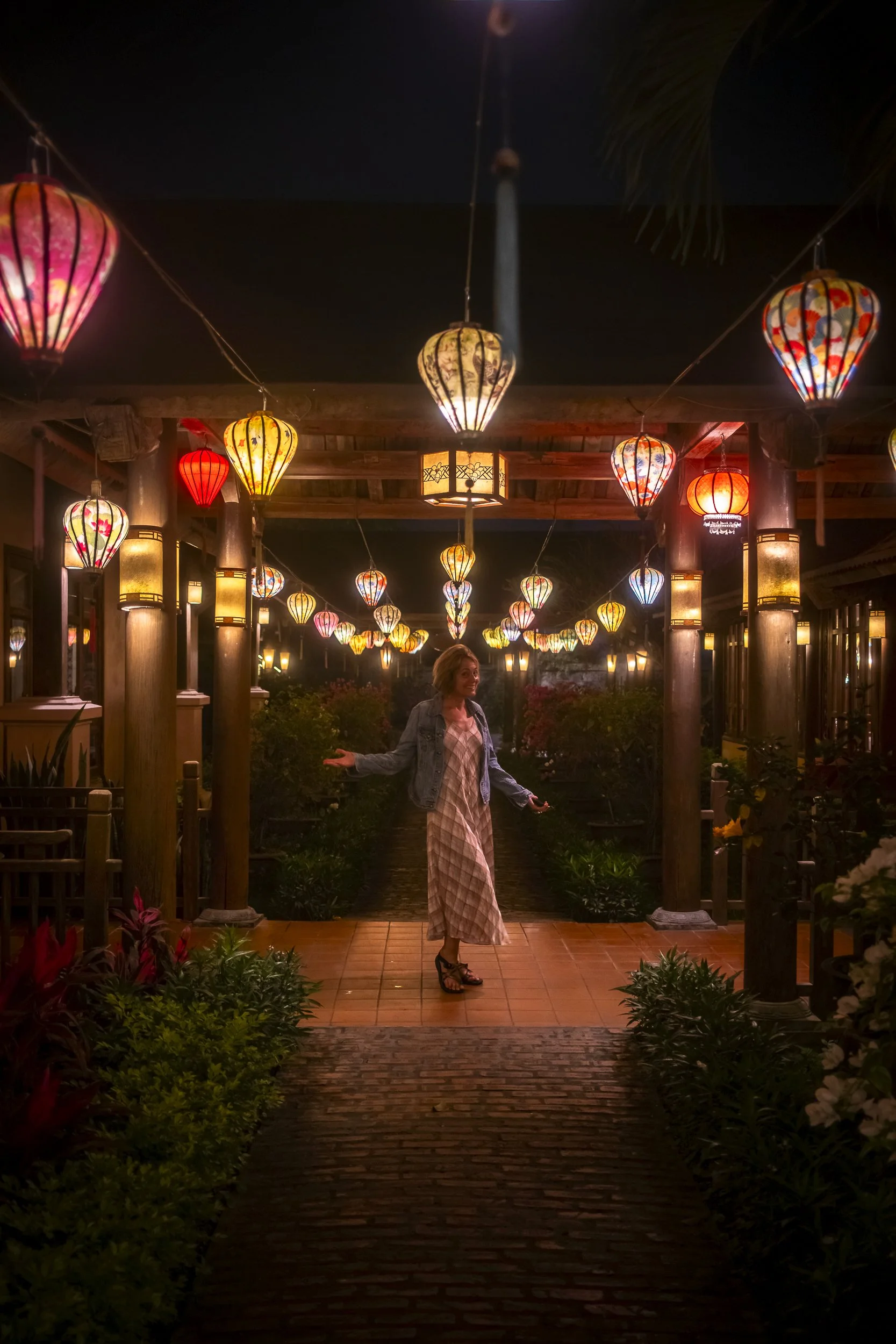 A woman standing under hanging colorful lanterns at night in an outdoor setting.