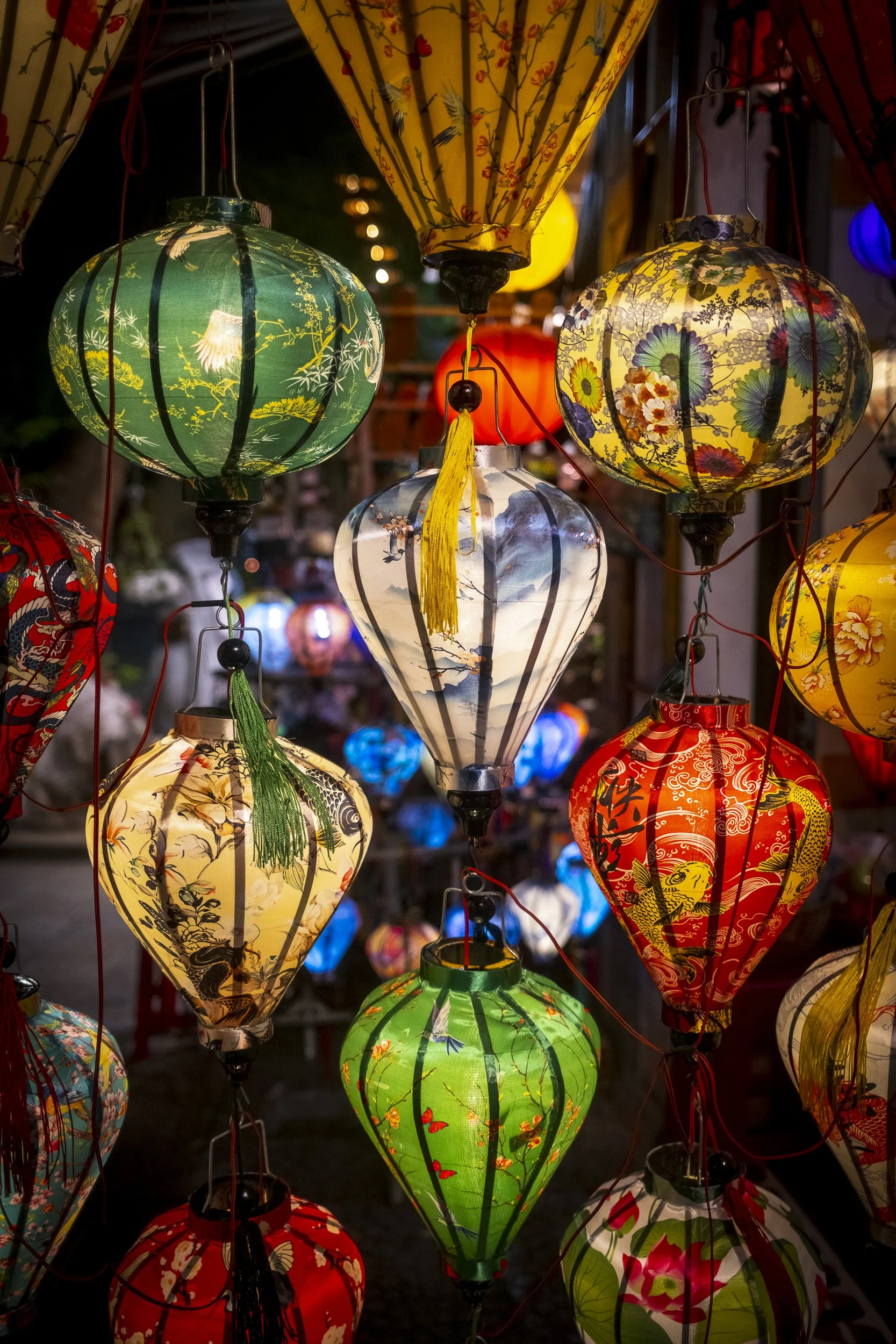 Colorful paper lanterns hanging at an outdoor market, illuminated at dusk.