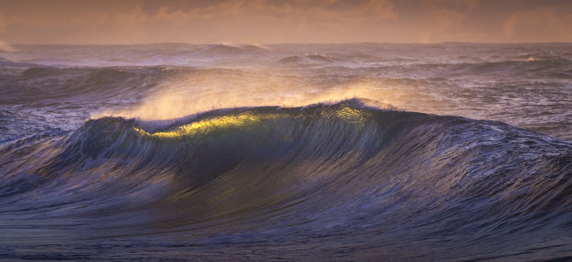 Sunset over ocean with large waves reflecting golden light