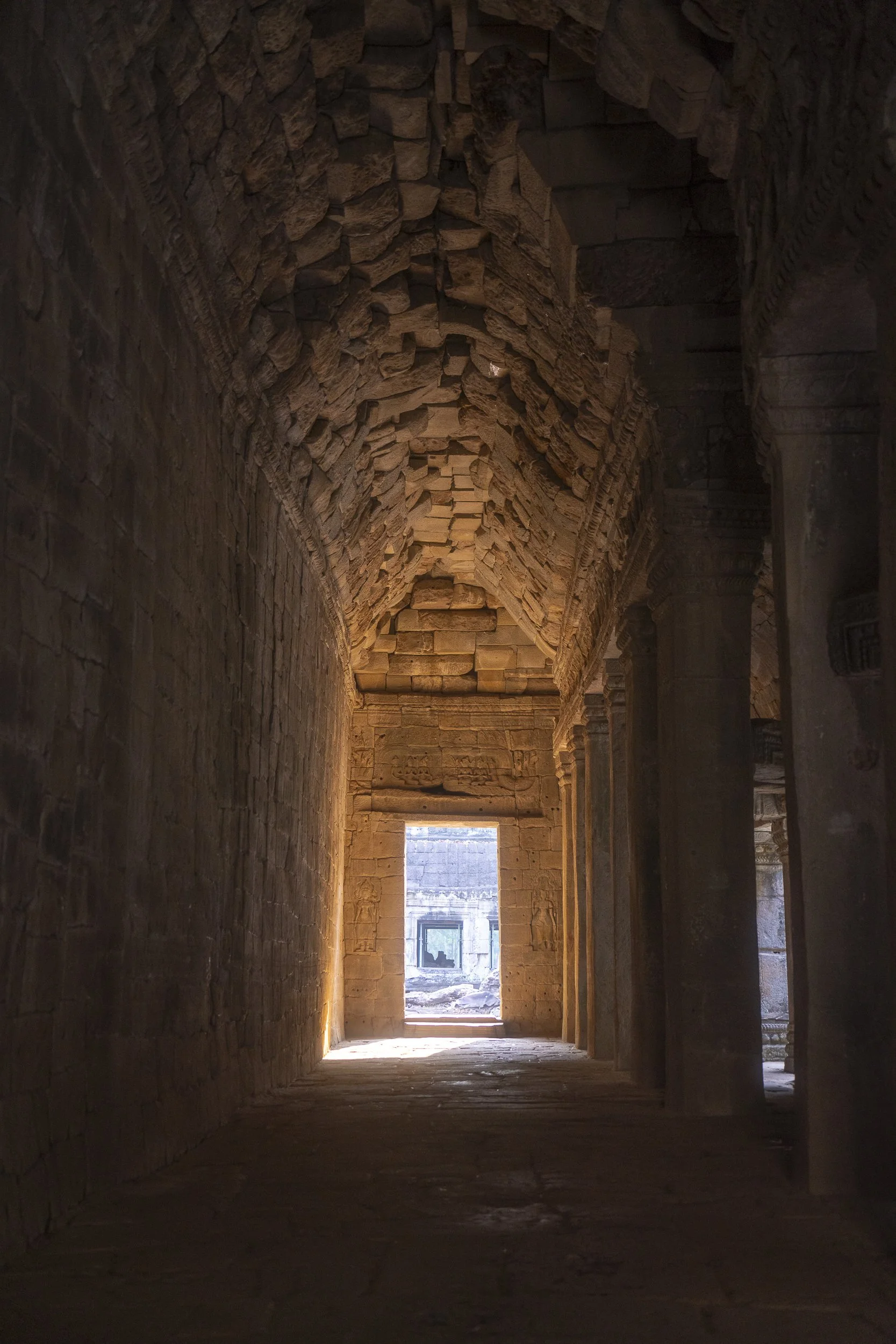Interior view of an ancient stone corridor with a vaulted ceiling, illuminated by natural light from an opening at the end.