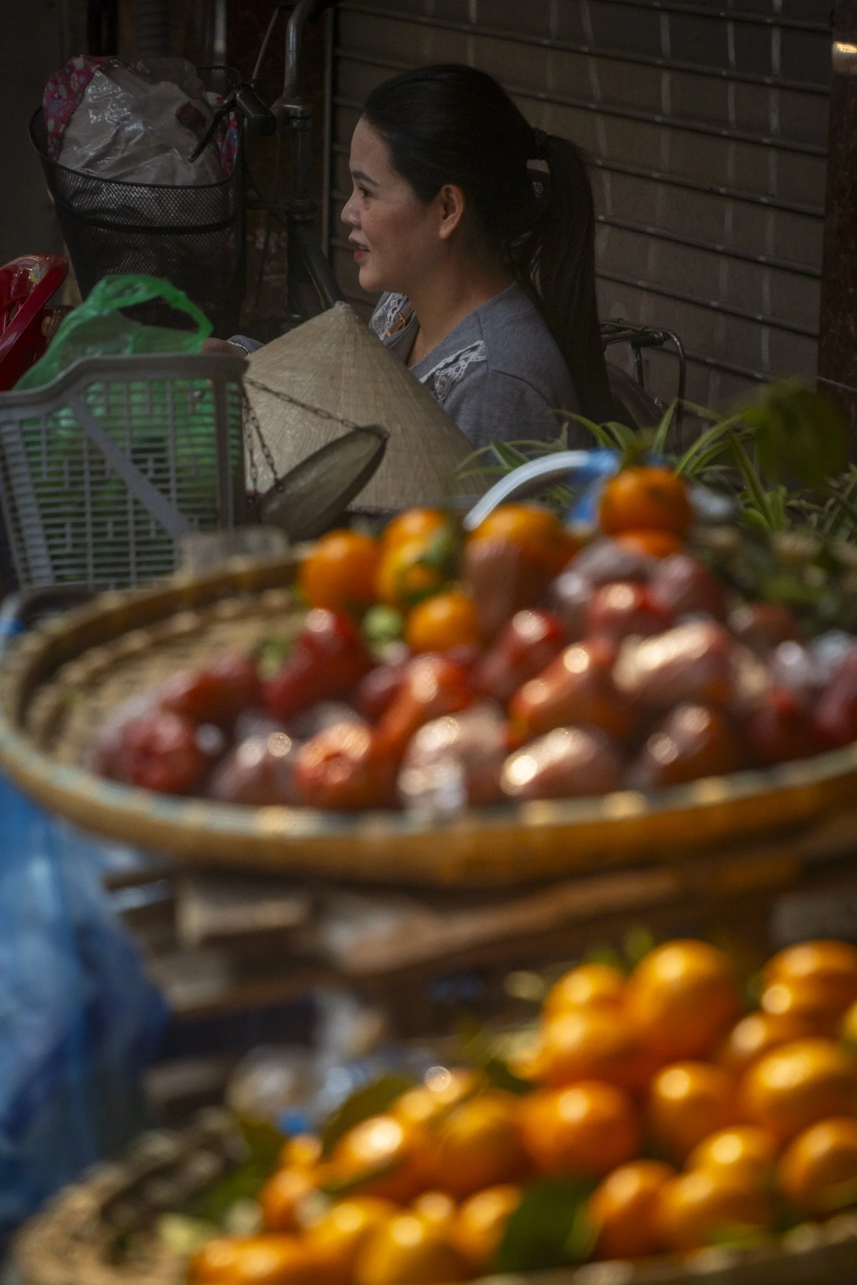 A woman standing behind a display of various fruits at an outdoor market, with oranges and other fruit in the foreground.