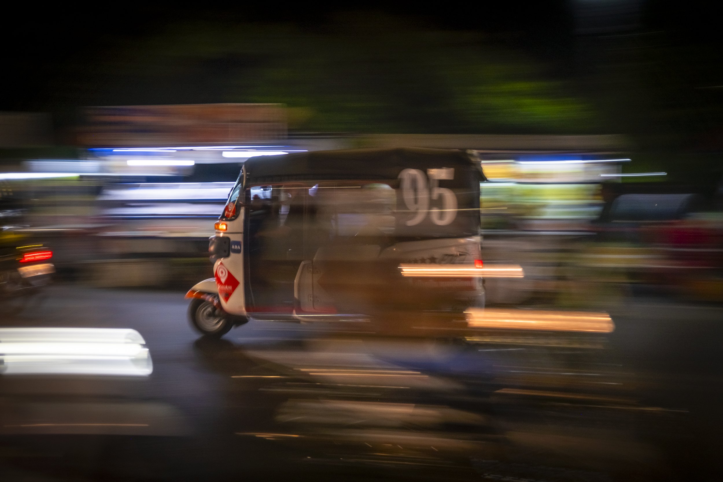 A tuk-tuk moving at night with motion blur and colored lights in the background.