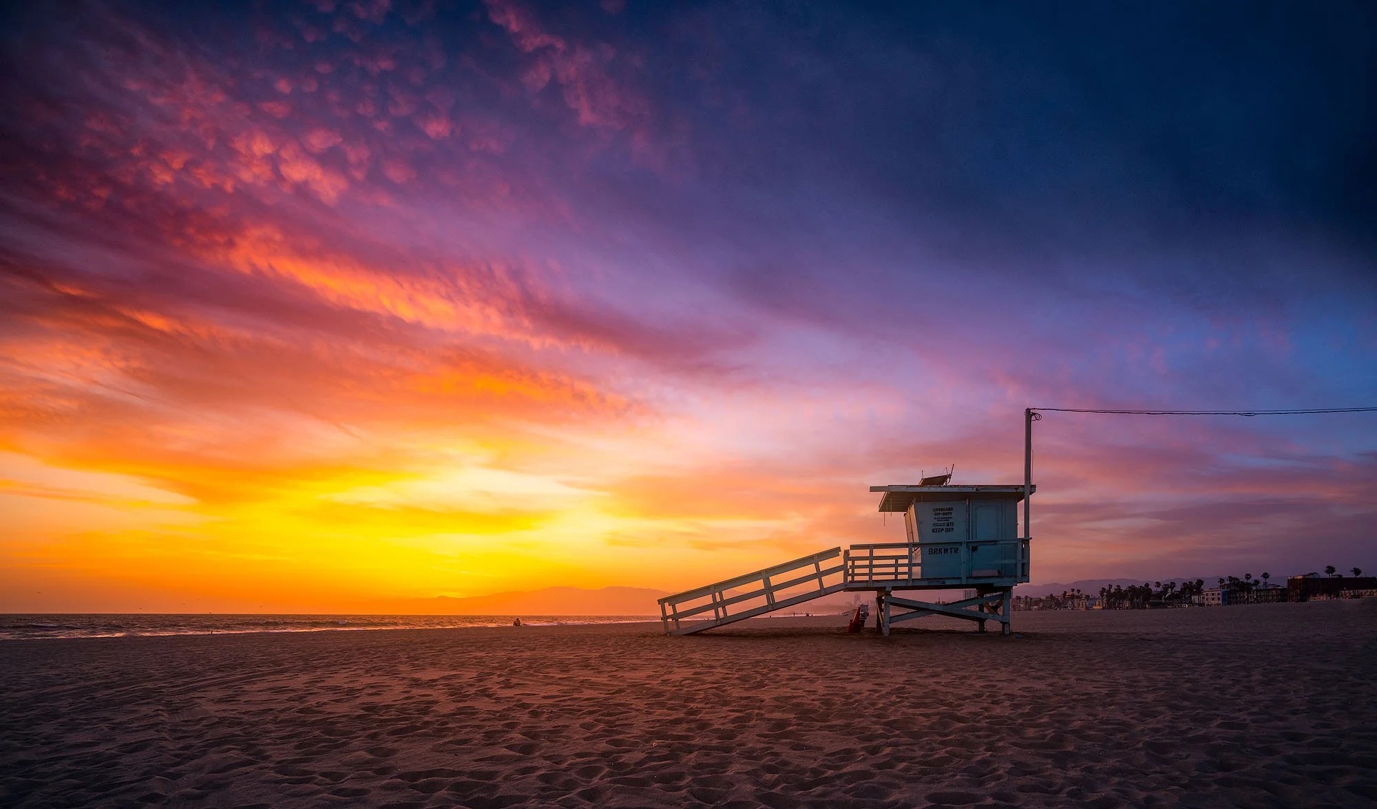 A lifeguard tower on a sandy beach at sunset with colorful clouds in the sky.