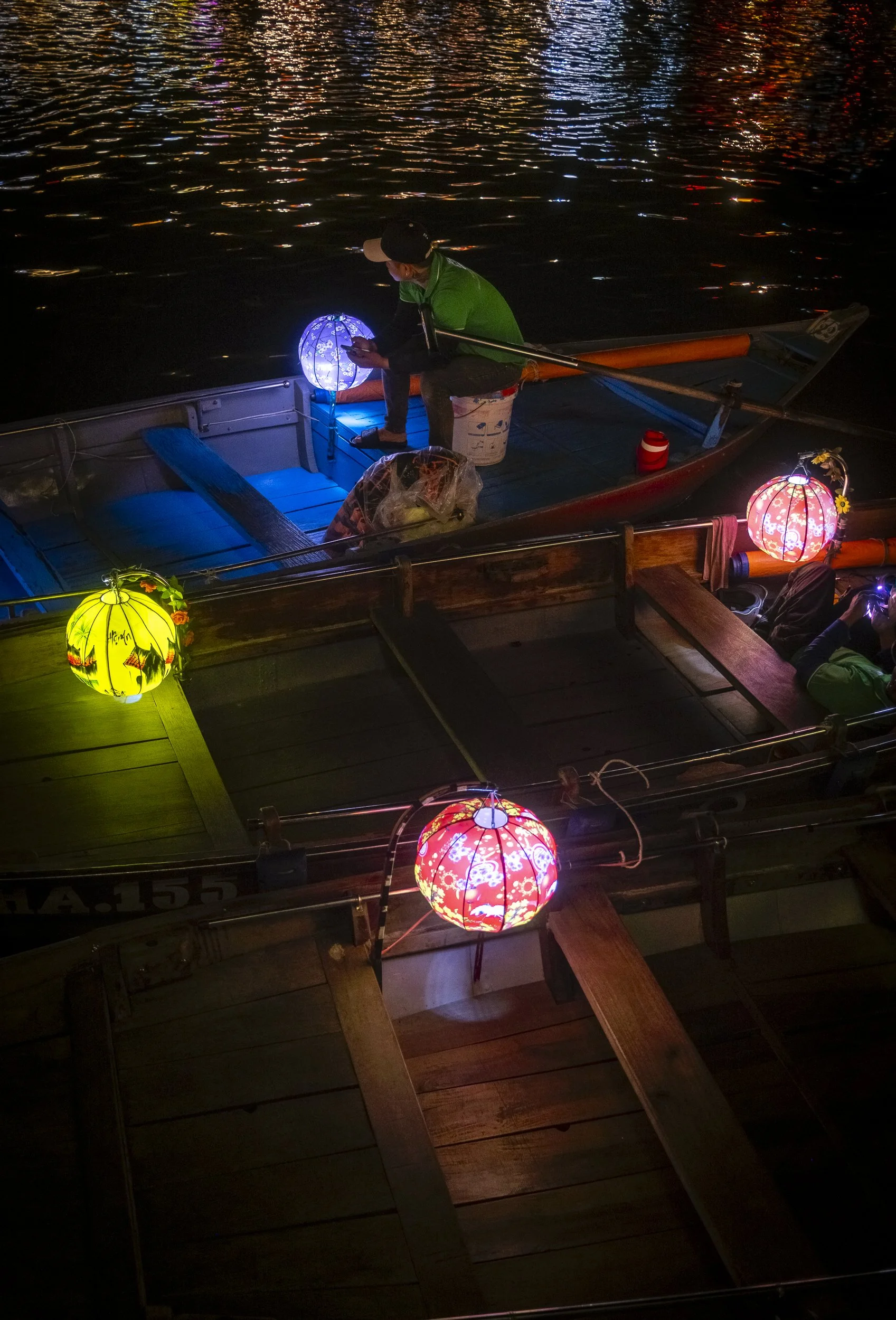 Boats docked on a river at night decorated with colorful lanterns, with reflection on the water.