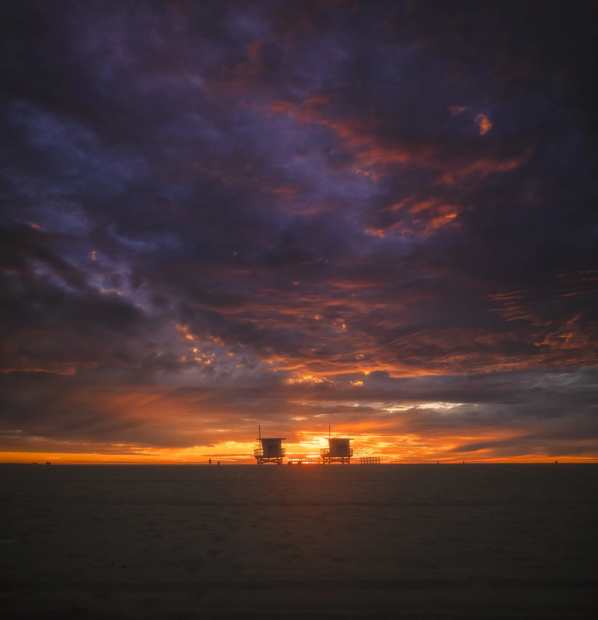 A sunset view over the ocean with colorful clouds and two lifeguard towers in the distance.