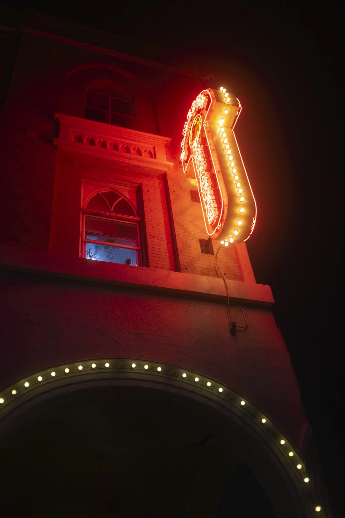 Nighttime photo of a building with a vertical neon sign that says "Restaurant" and the word "Chili" at the top, illuminated in red with lights, mounted on an exterior brick wall.