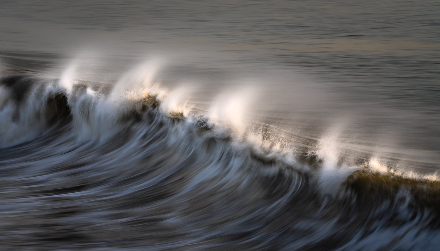 Waves breaking in the ocean with white foam and smooth, blurred water movement.