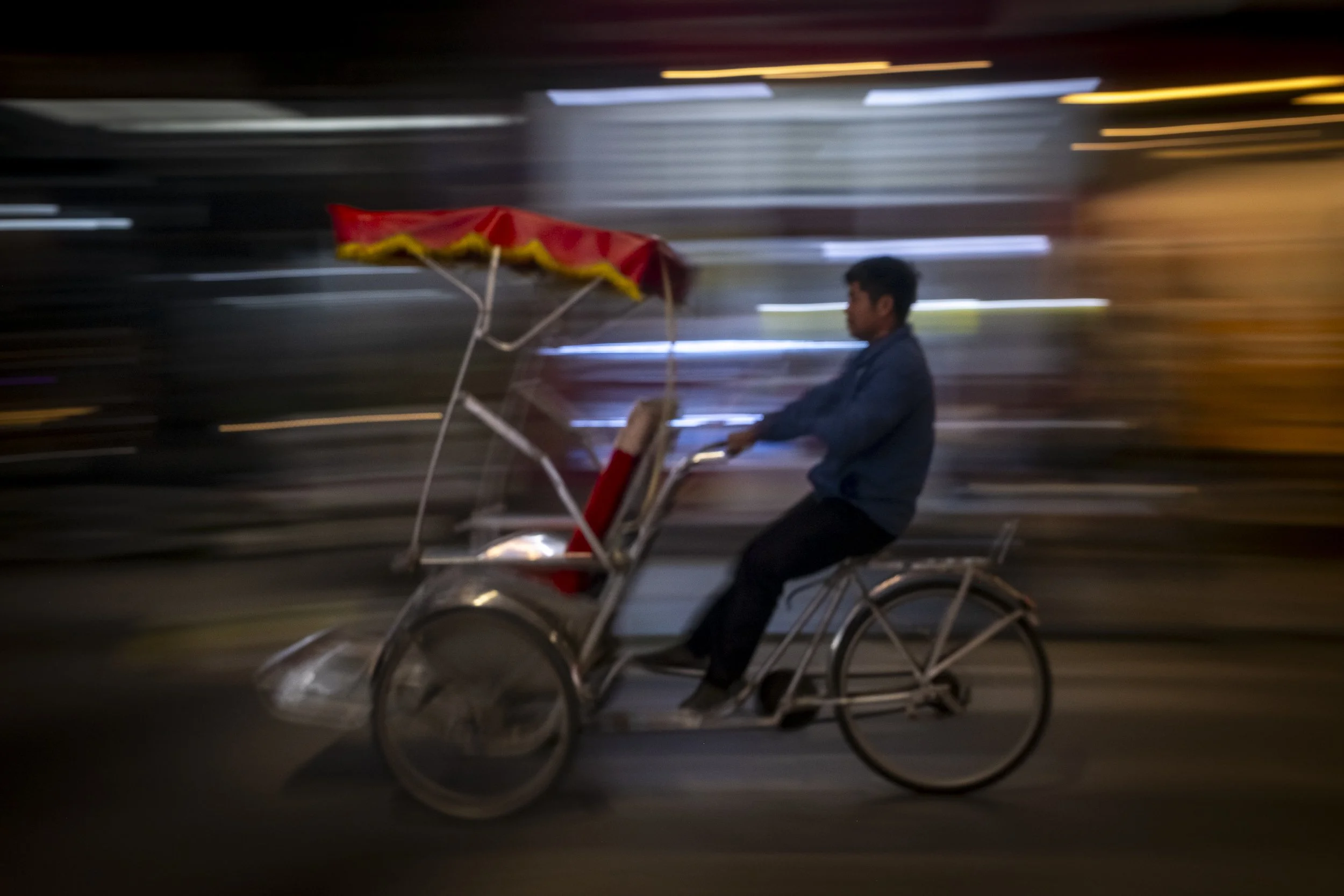 A man riding a cycle rickshaw at night with motion blur background.