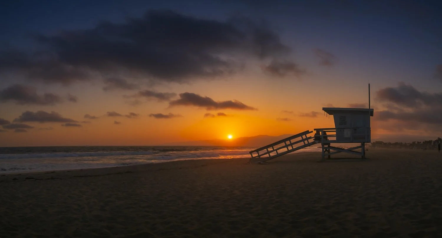 Sunset at the beach with a lifeguard tower and cloudy sky.