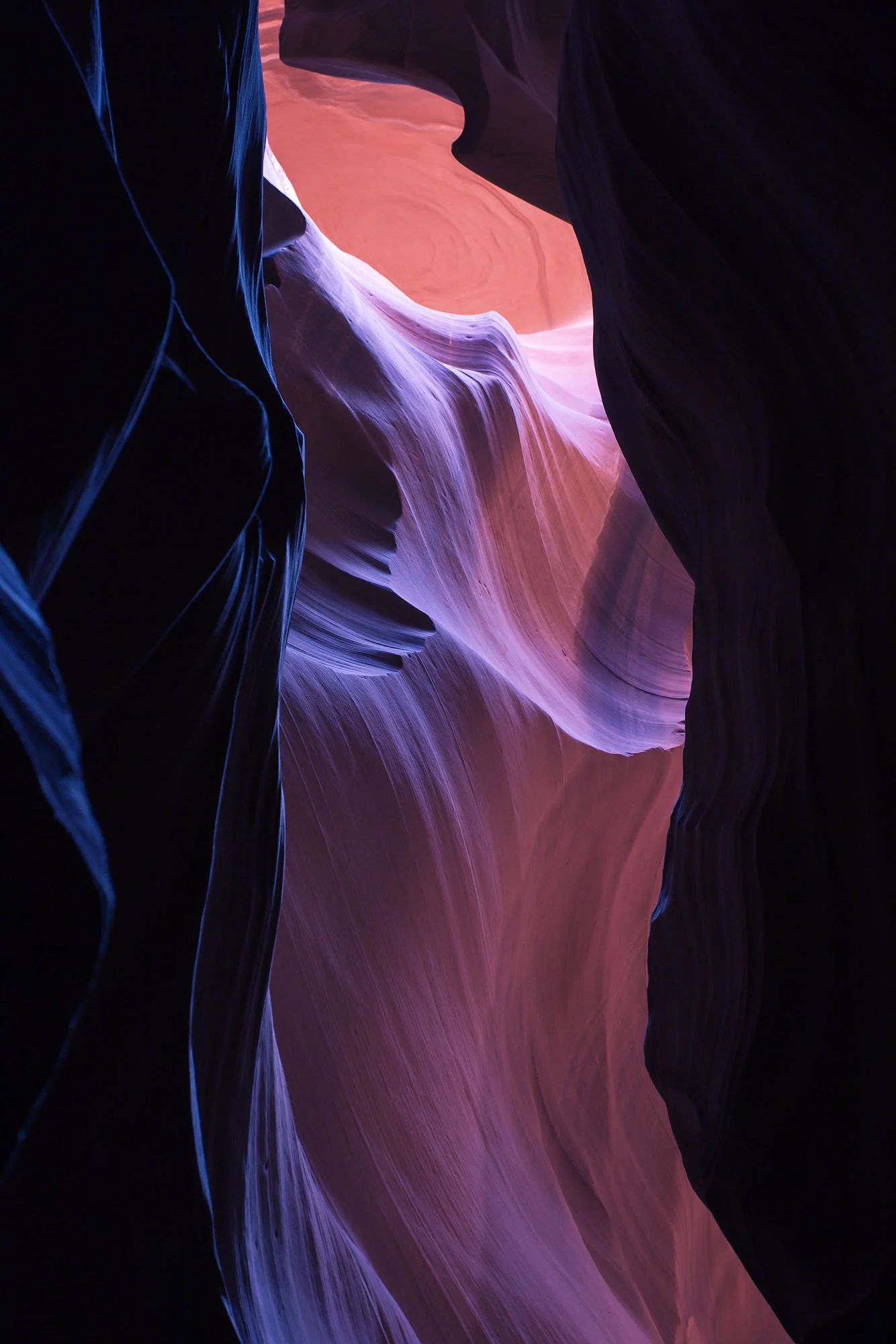 Colorful layered rock formations in a narrow canyon with smooth, flowing shapes and shades of purple, pink, and orange.