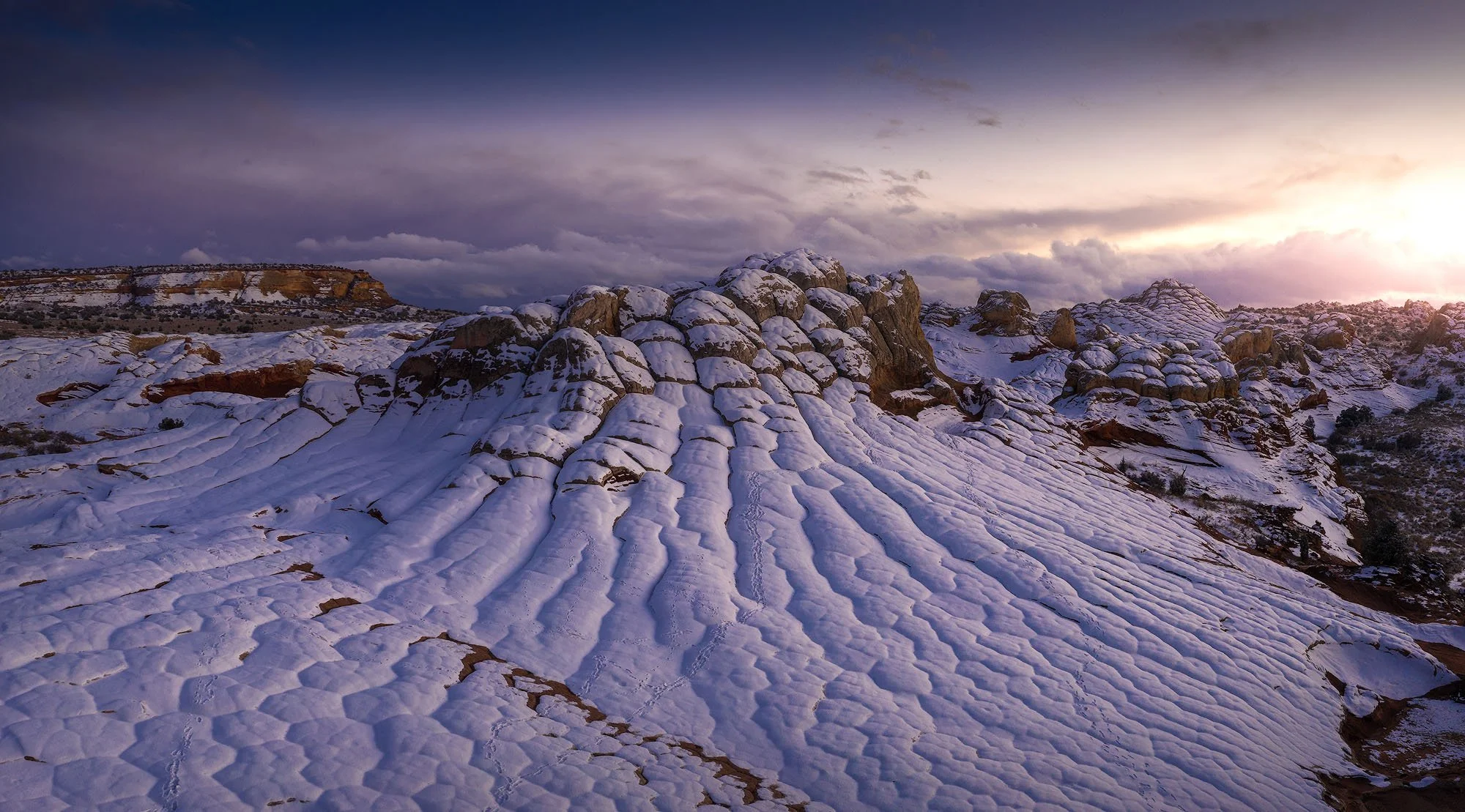 Snow-covered rock formations and desert landscape at sunset in a mountainous area.