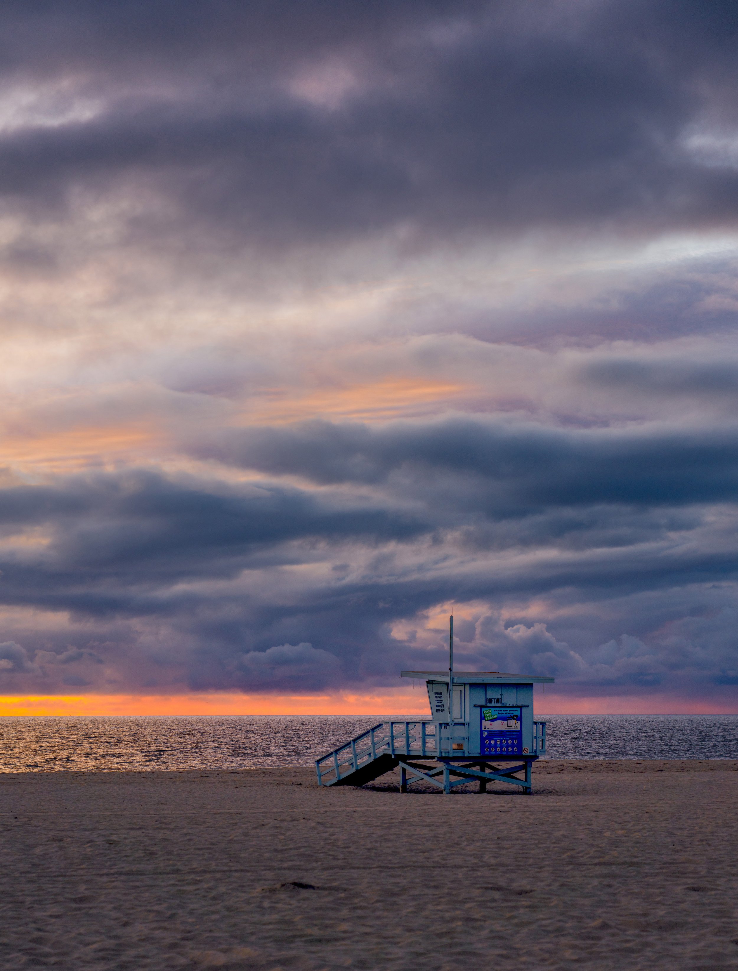 A lifeguard tower on a sandy beach during sunset with dramatic dark clouds in the sky.