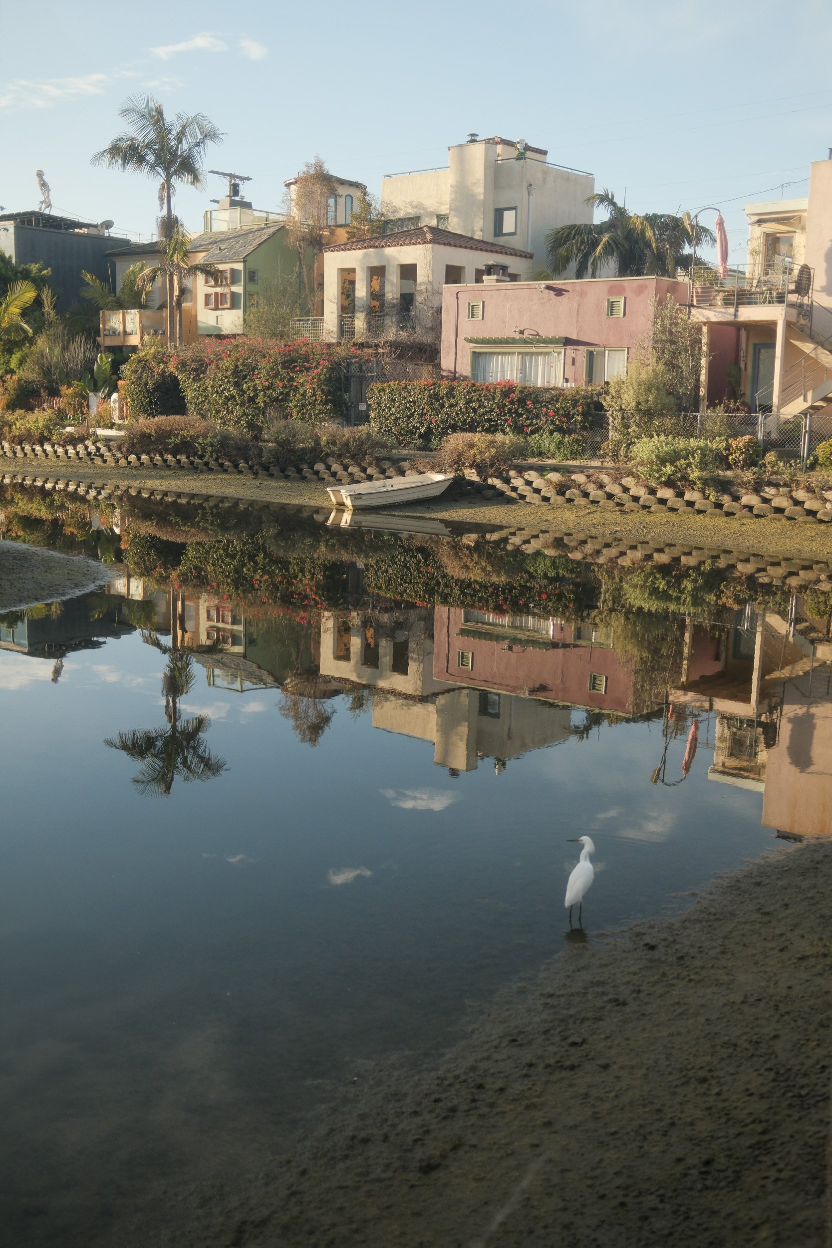 Colorful houses along a waterway with a boat and a white heron standing at the water's edge, reflected in the water under a clear blue sky.