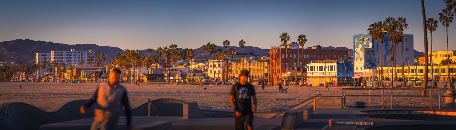 Beach with palm trees, colorful buildings, and mountains in the background during sunset.