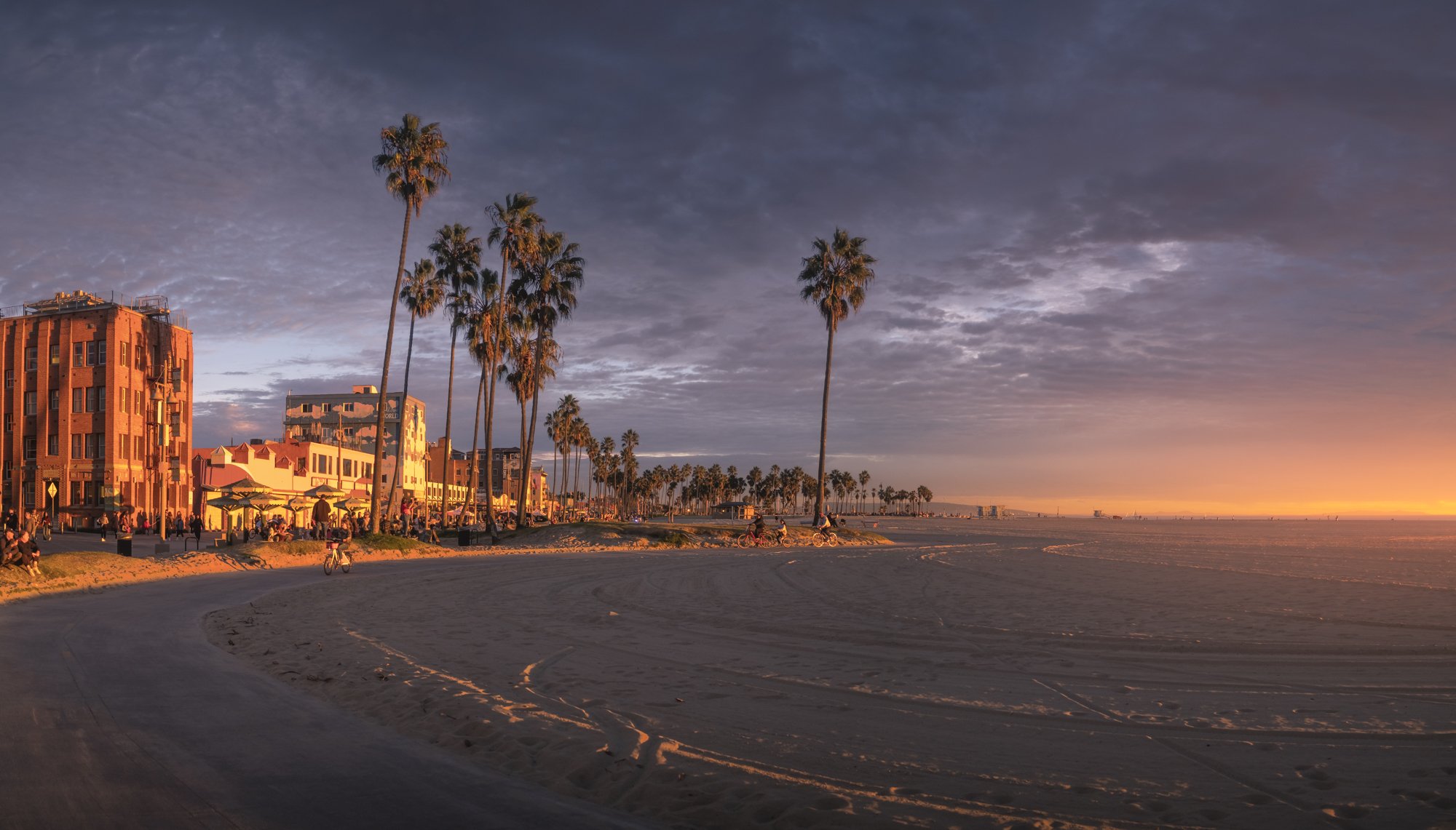 Sunset over a beach in Venice, California, with palm trees, colorful sky, and buildings along the shoreline.