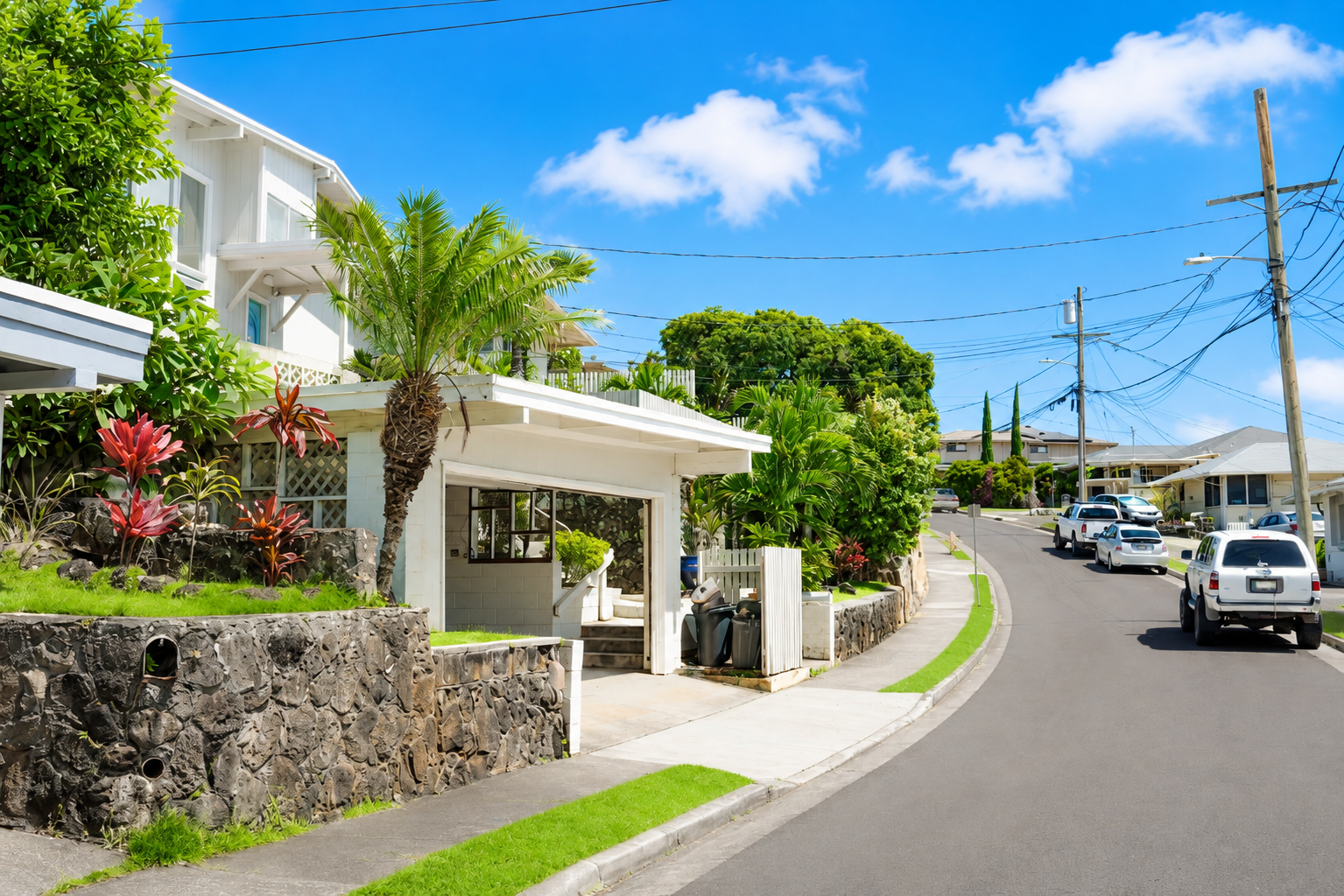 Residential street with white houses, lush greenery, and a clear blue sky.