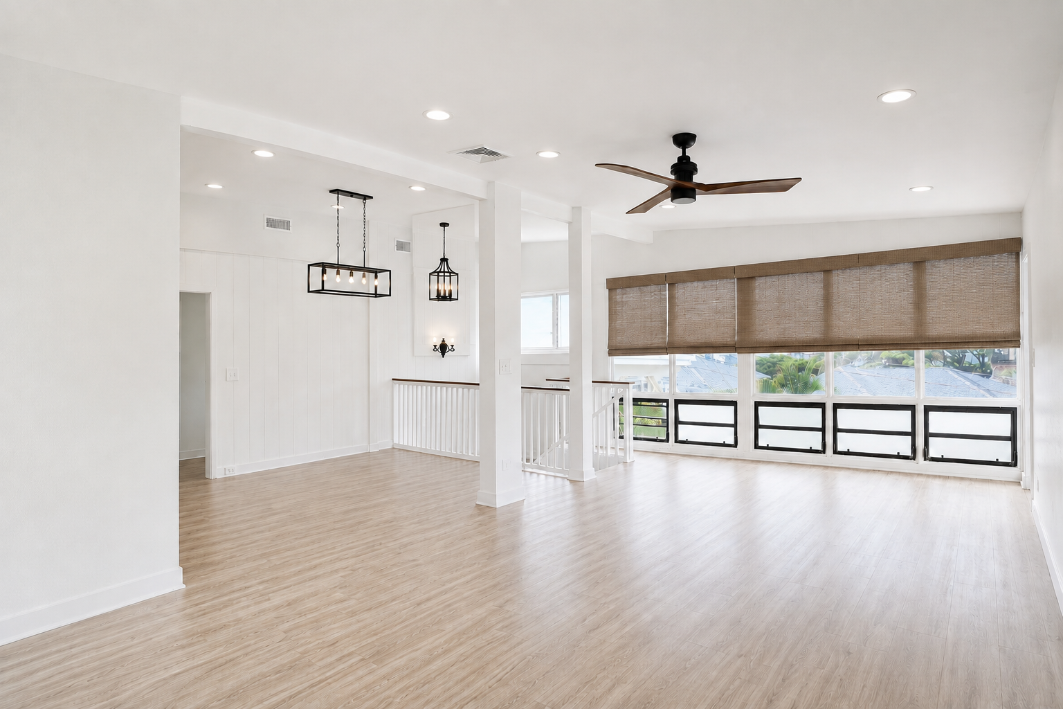 Hawaii Real Estate Photography:  Empty living room with large windows, beige roller blinds, light wood flooring, white walls, ceiling fan, and modern lighting fixtures.