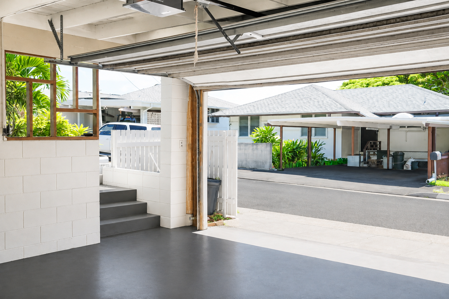 View from inside a garage looking out onto a driveway and neighboring house with greenery