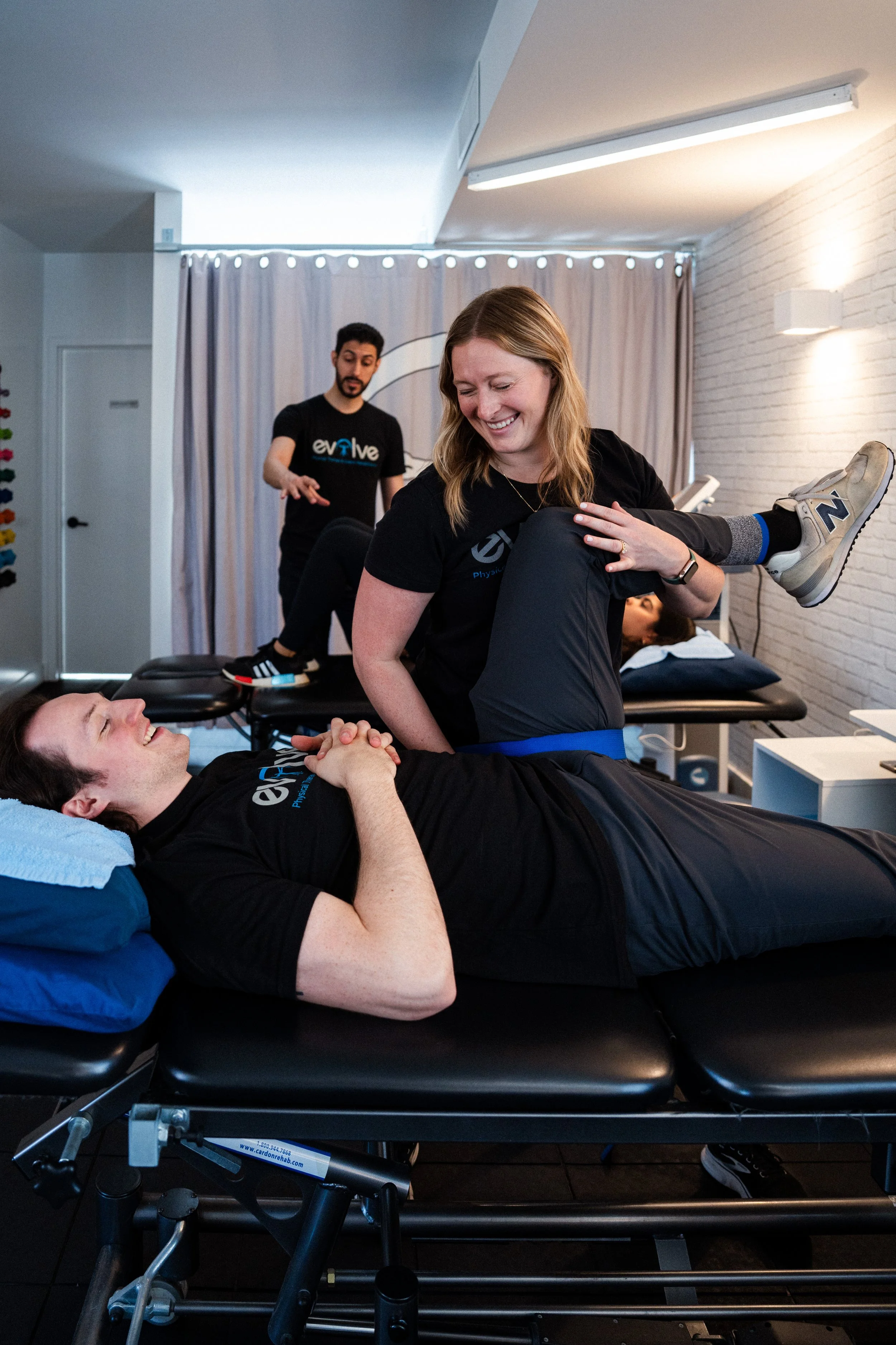 A physical therapist assisting a patient with leg exercises on a treatment table in a therapy clinic.