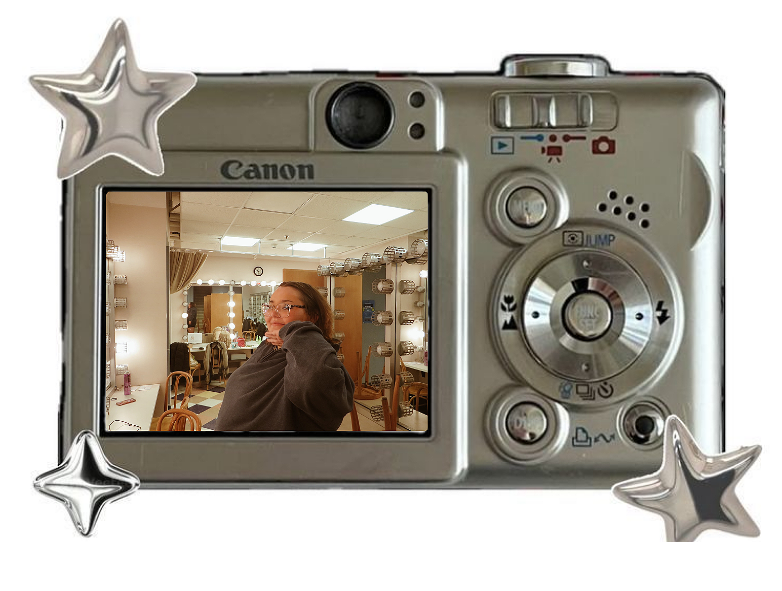Silver camera with playful star-shaped decorations on corners, showing a woman in a dressing room or makeup area reflected in its screen.