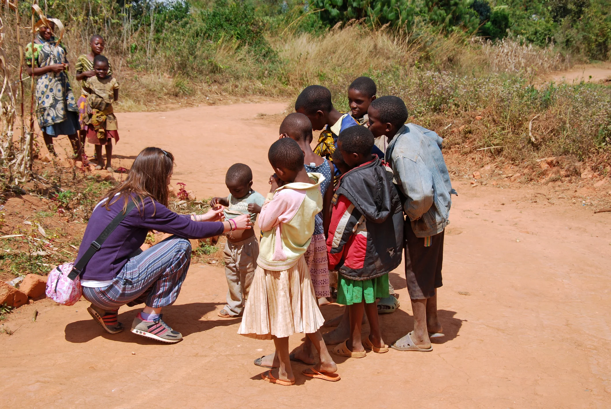A woman crouches down helping a young kid on a dirt road