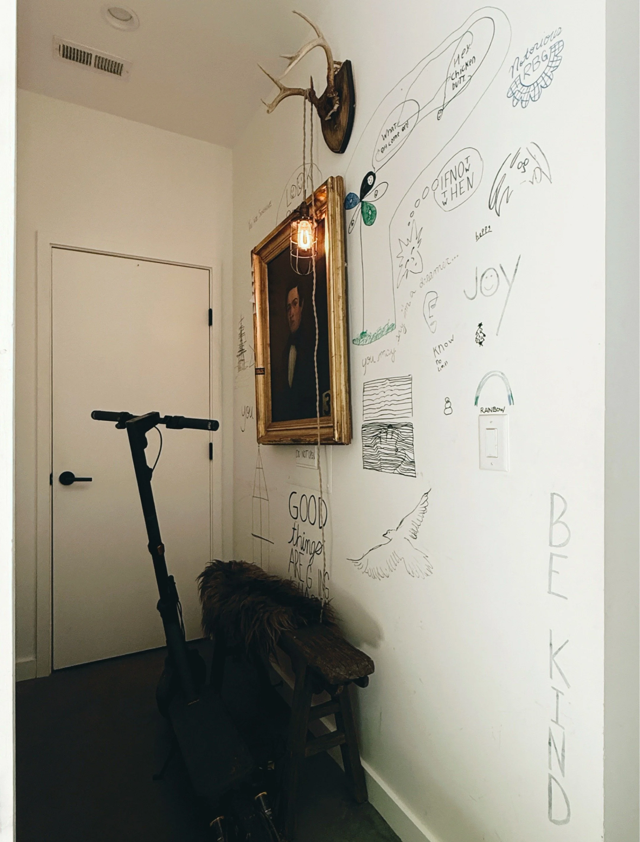 Hallway wall covered in children's drawings and doodles with antique portrait and scooter