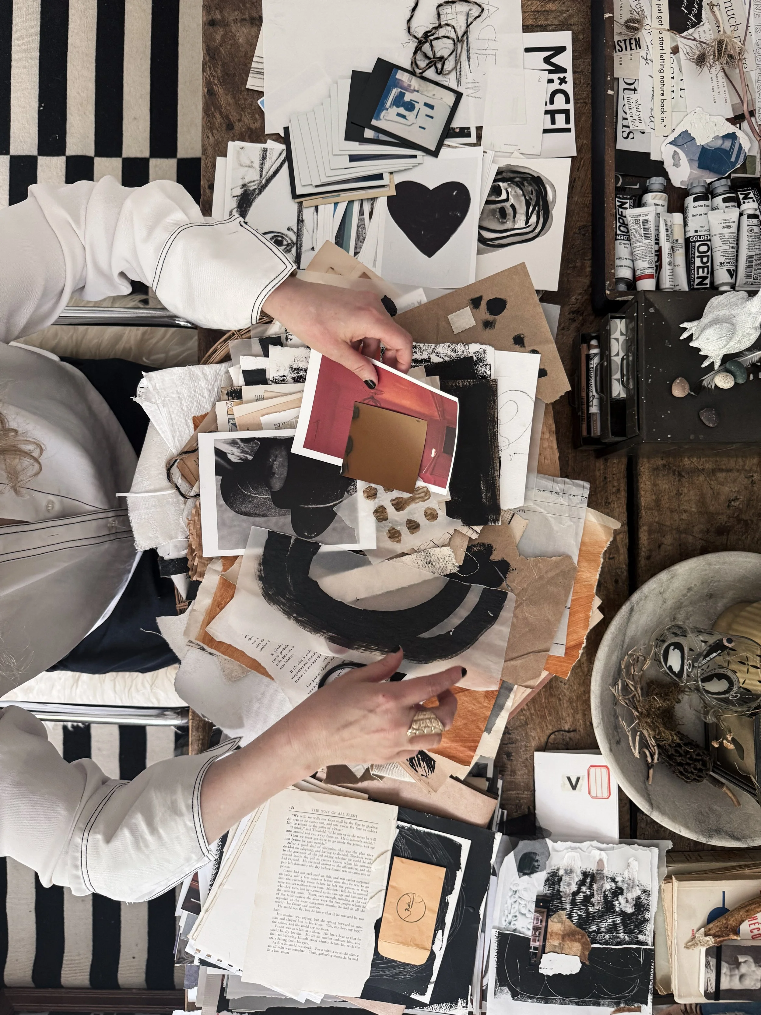 Artist working with mixed media collage materials, photographs and paper arranged across a studio worktable.