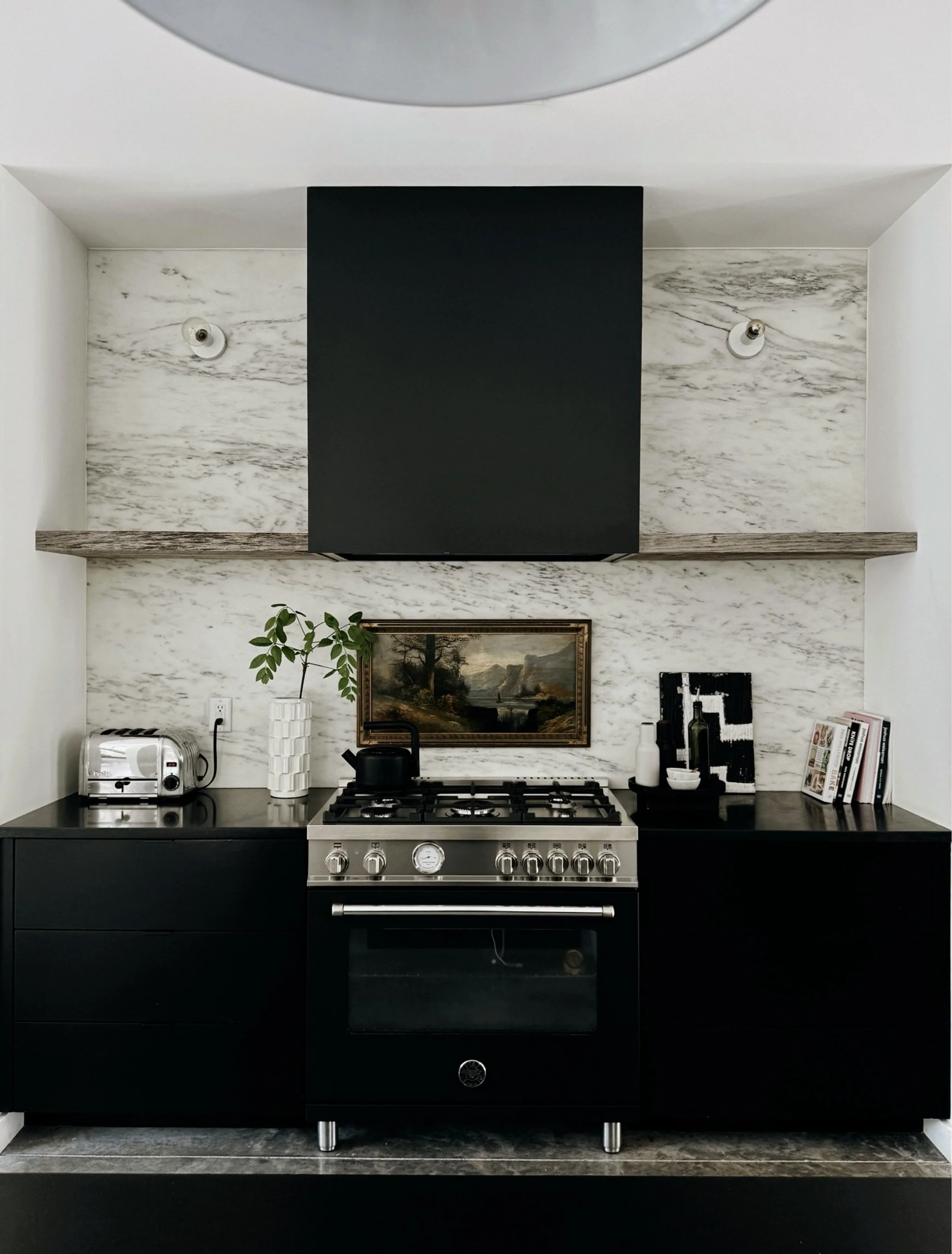modern kitchen with black cabinets, marble wall, reclaimed wood shelves with black range, modern and vintage art mix. from the home of artist michel van devender in charlotte, nc.