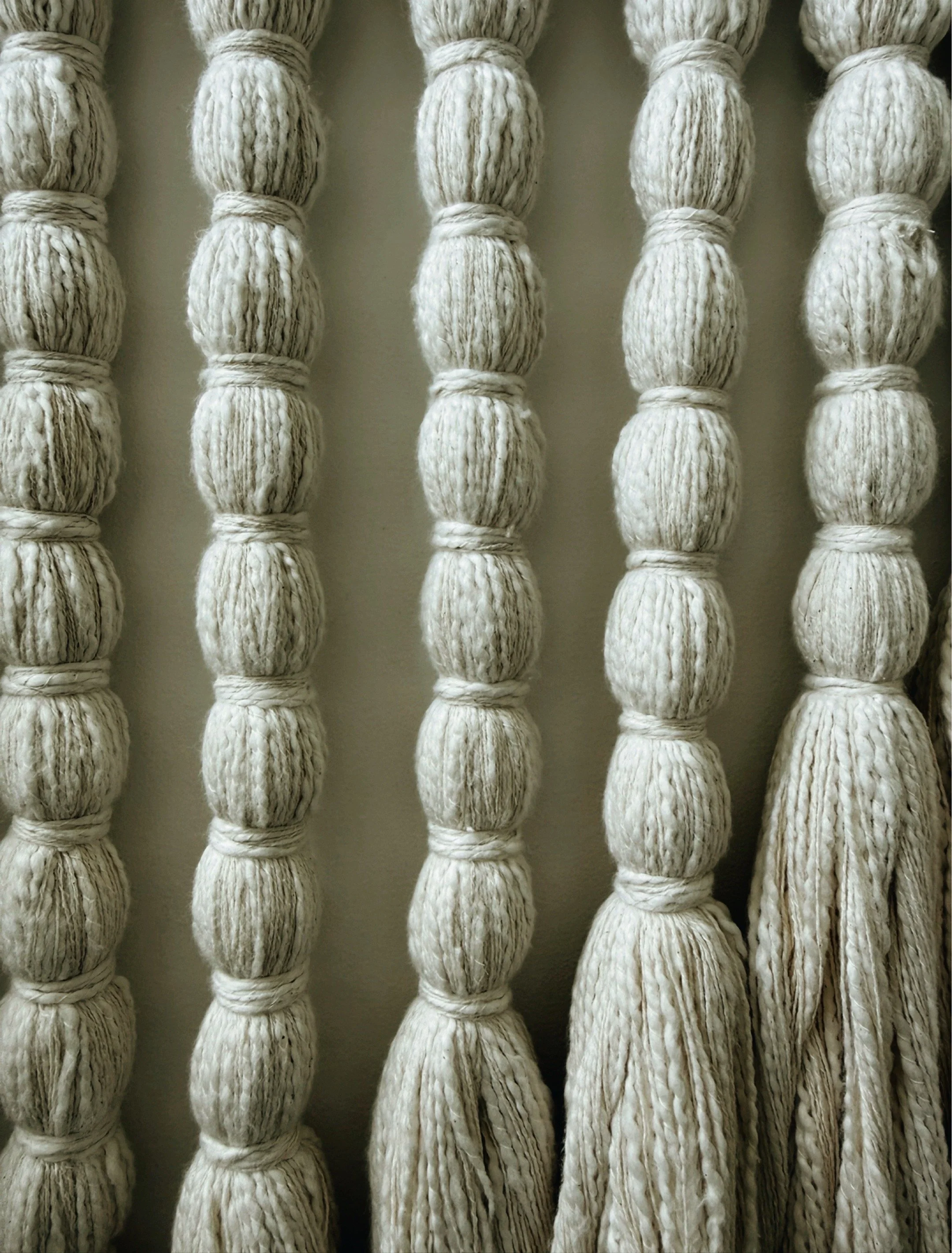 Close up of cream fiber art wall hanging with repetitive knotted texture and tassel ends