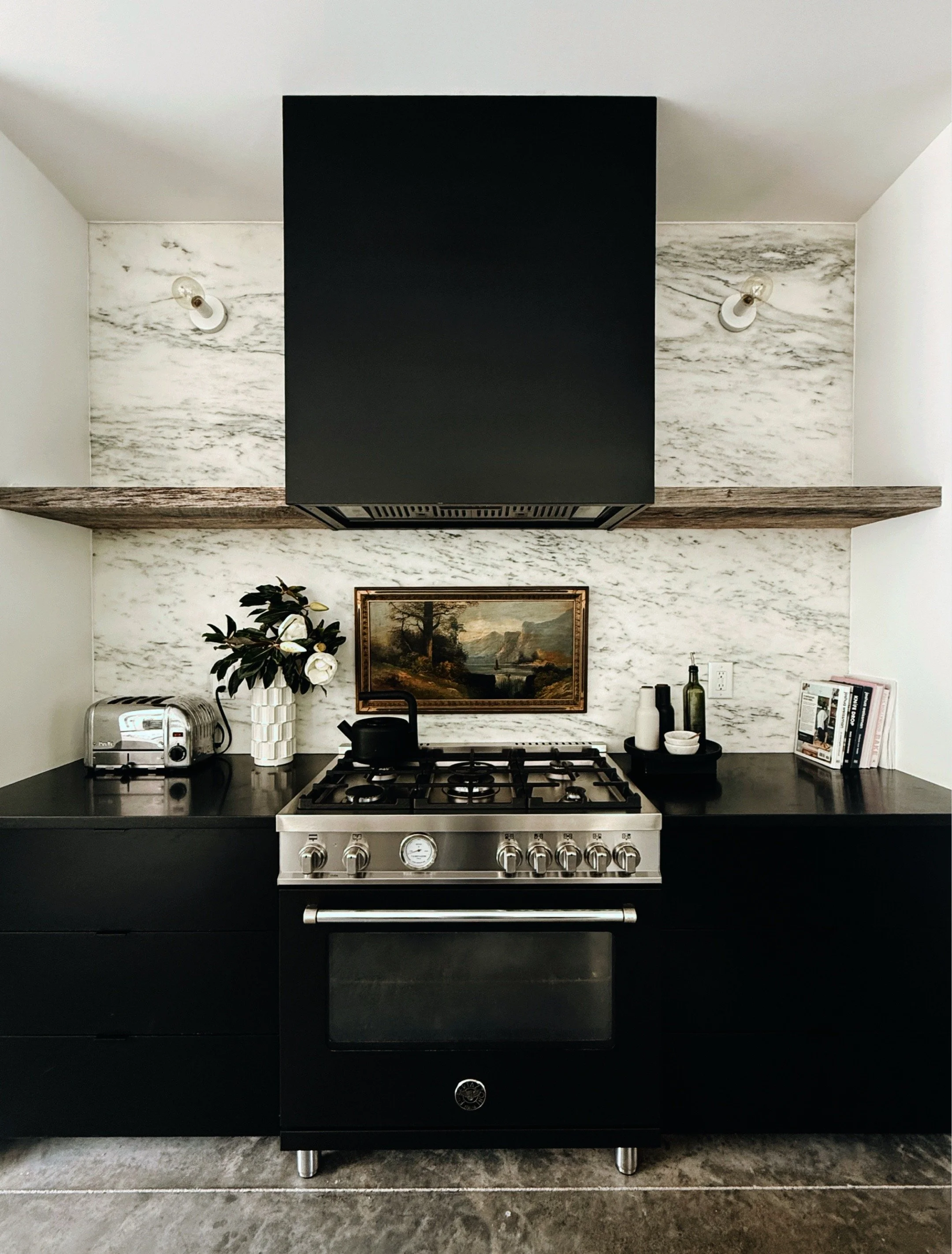 Black kitchen cabinets and counter with fresh flowers in glass vases, fruit, and everyday objects arranged in natural light.