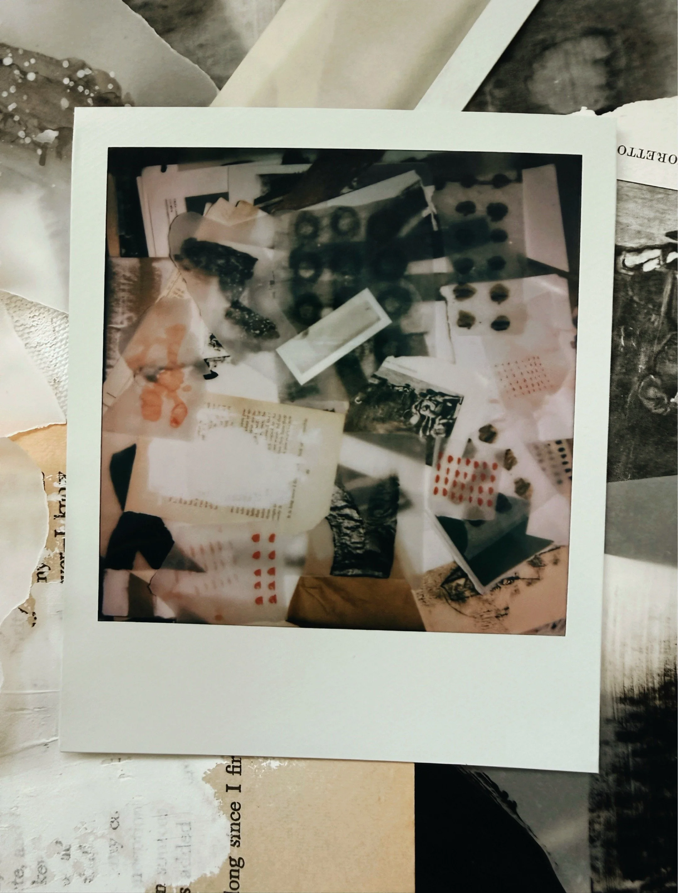 Polaroid photograph of studio collage materials, papers, marks and fragments scattered across a work surface