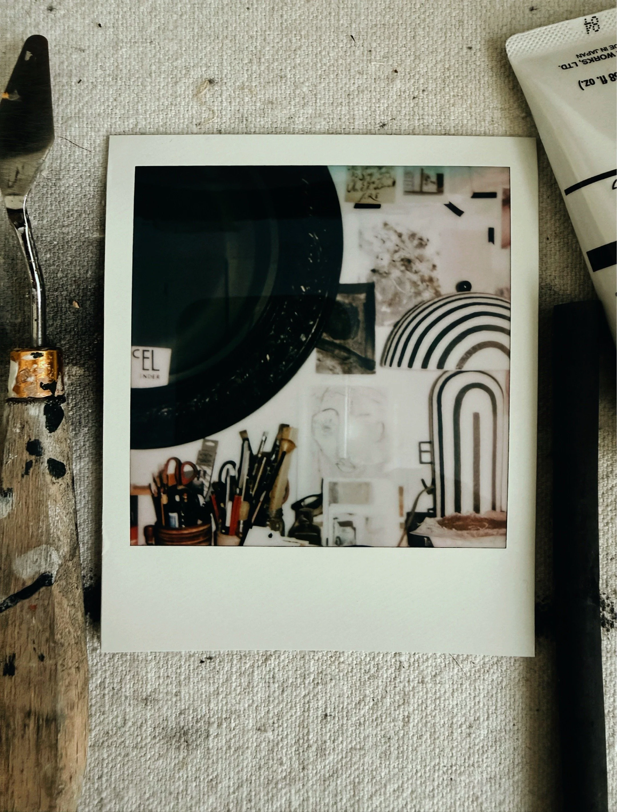 Polaroid photograph of Michel Van Devender's art studio showing a round mirror, paint brushes, and pinned references including arch imagery