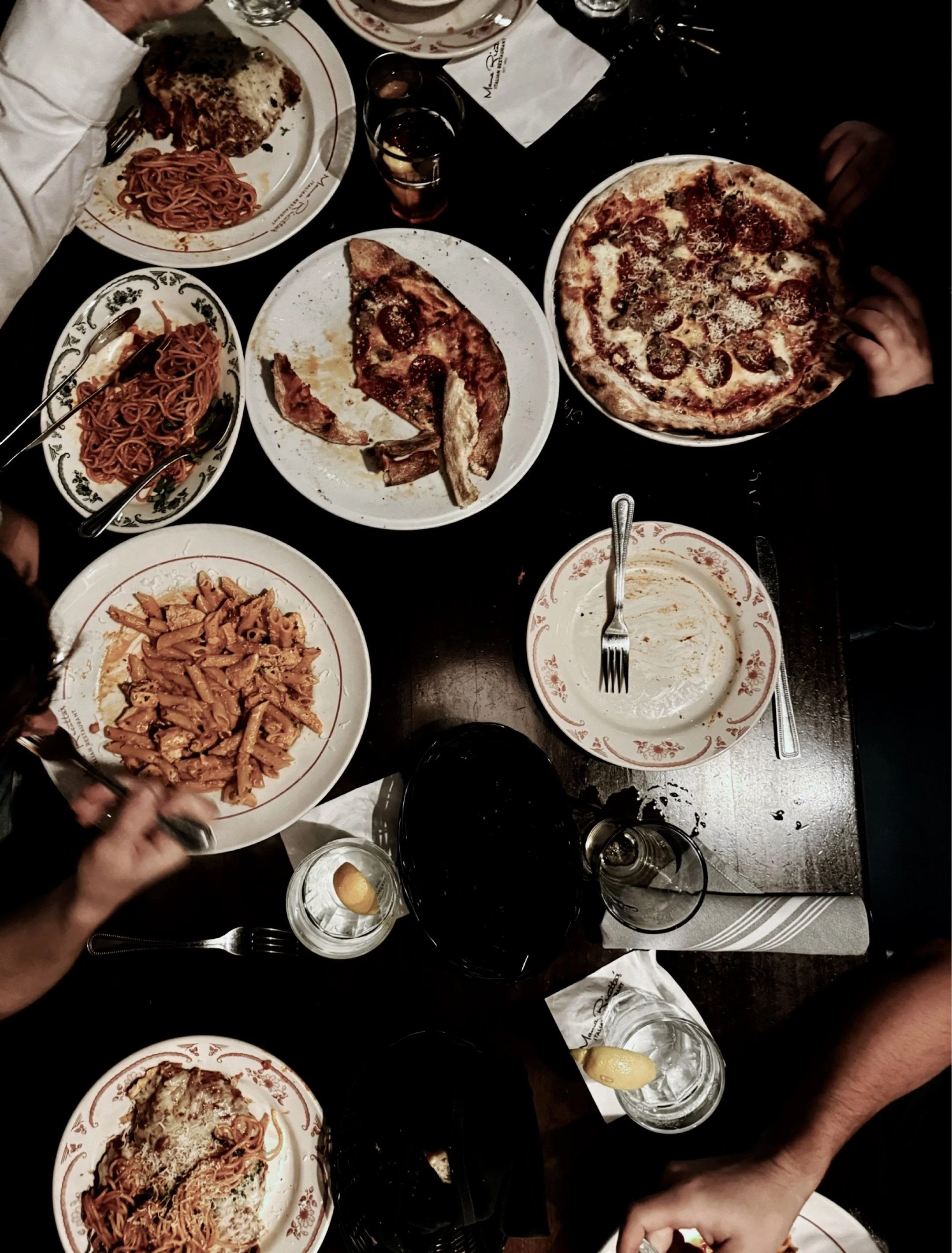 Overhead view of Italian family dinner table with pasta pizza and hands reaching in dark moody light