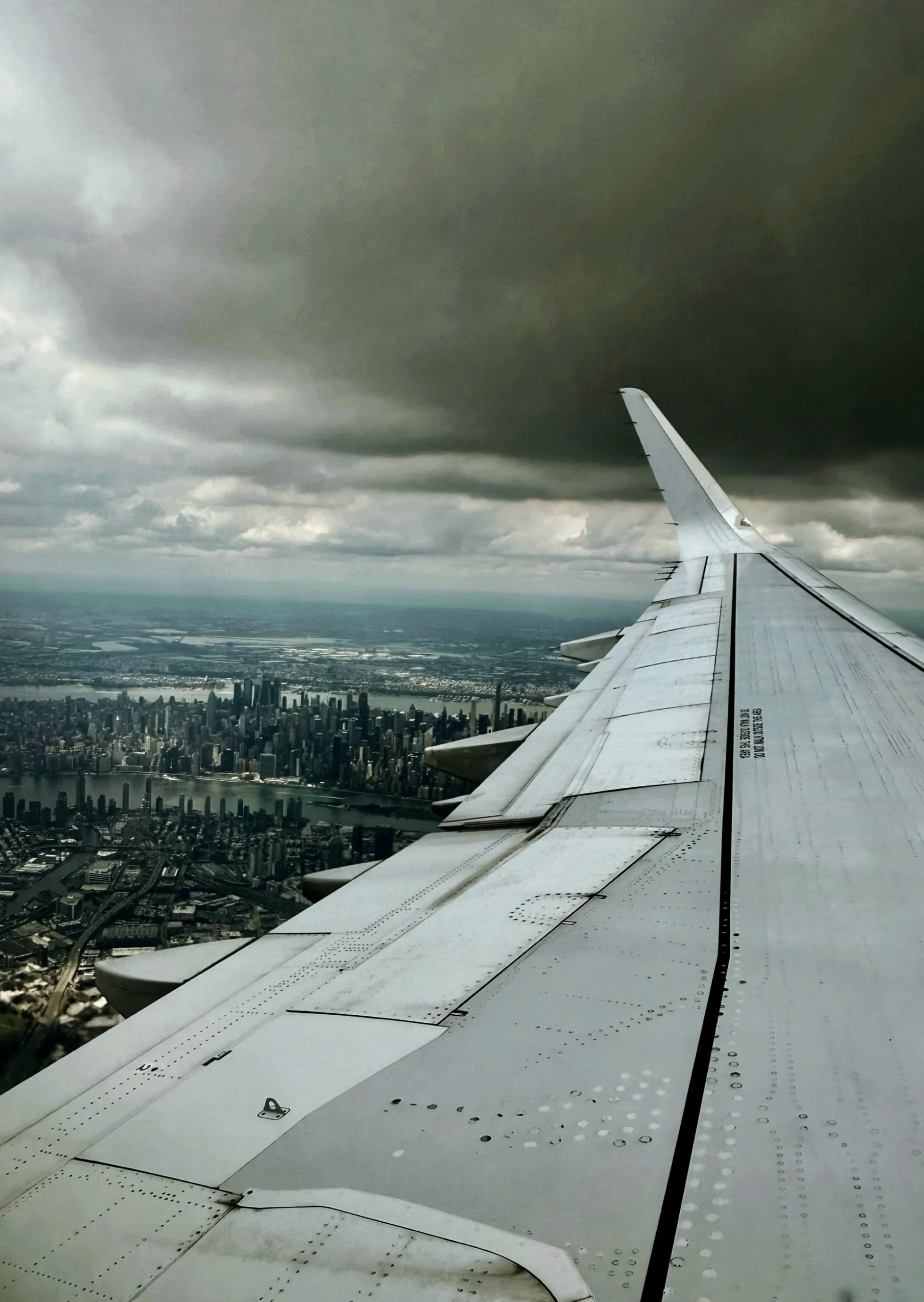 Airplane wing above Manhattan and storm clouds during arrival into New York City.