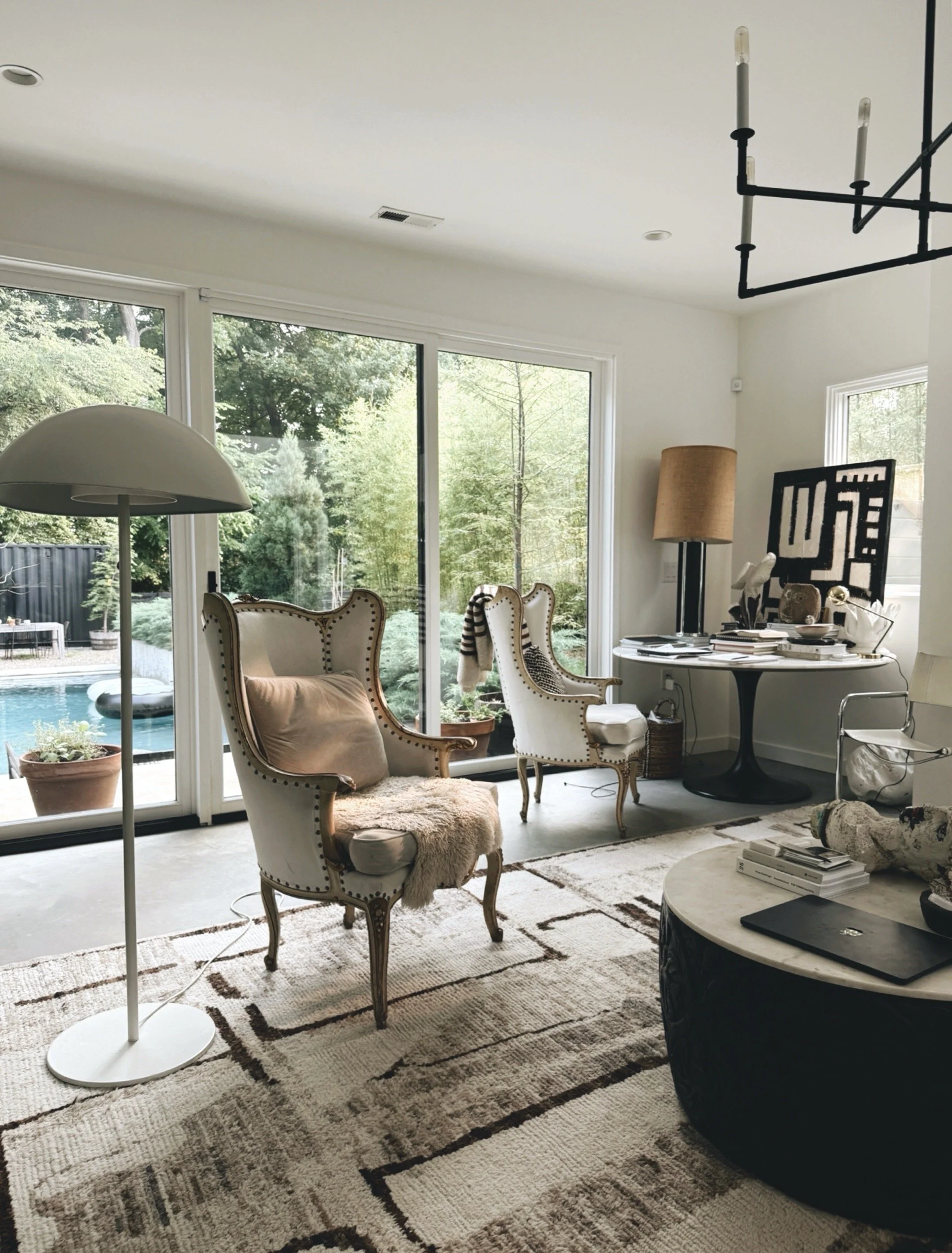 Light filled living room with vintage wingback chairs, contemporary artwork, and floor to ceiling windows overlooking a garden. From the home of artist and psychotherapist Michel Van Devender.