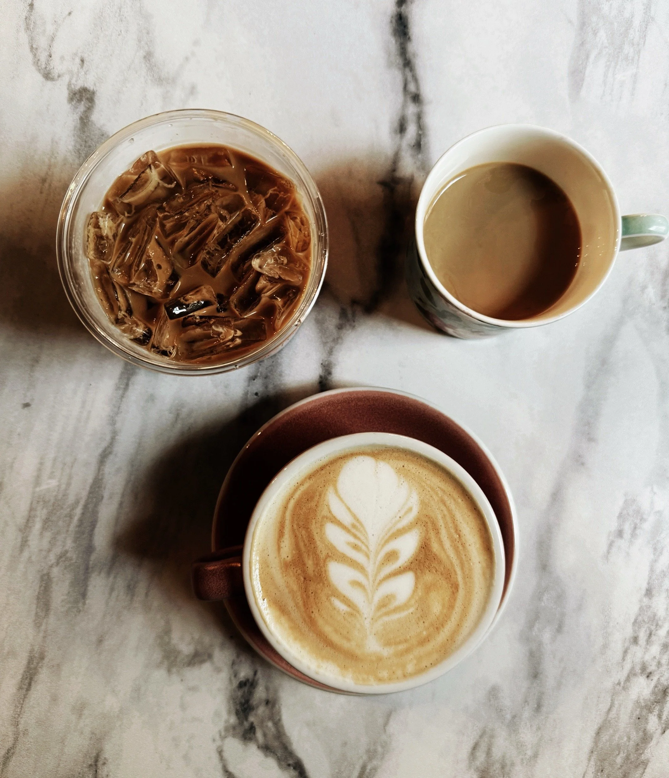 Overhead view of three coffees on marble table including iced coffee and latte art at local cafe