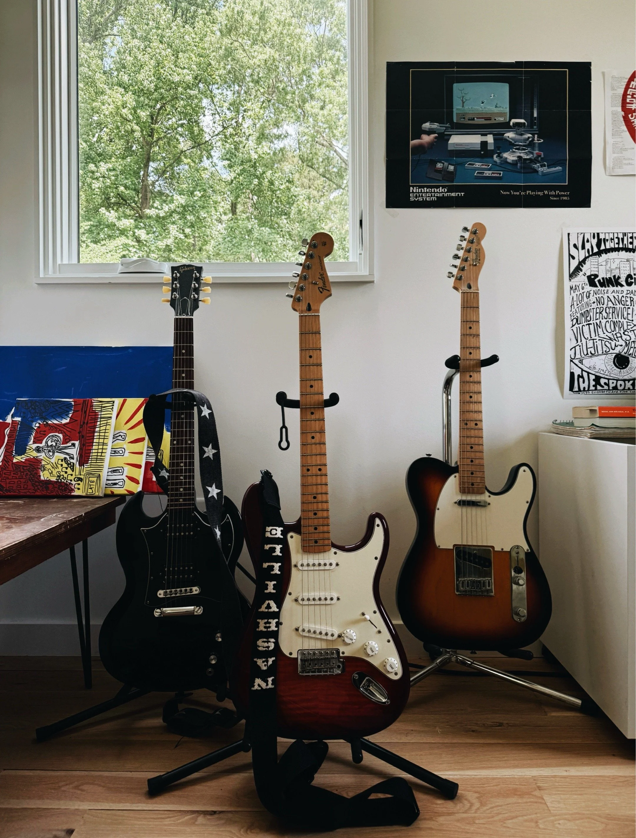 Three electric guitars on stands in a music room with Nintendo poster and colorful artwork