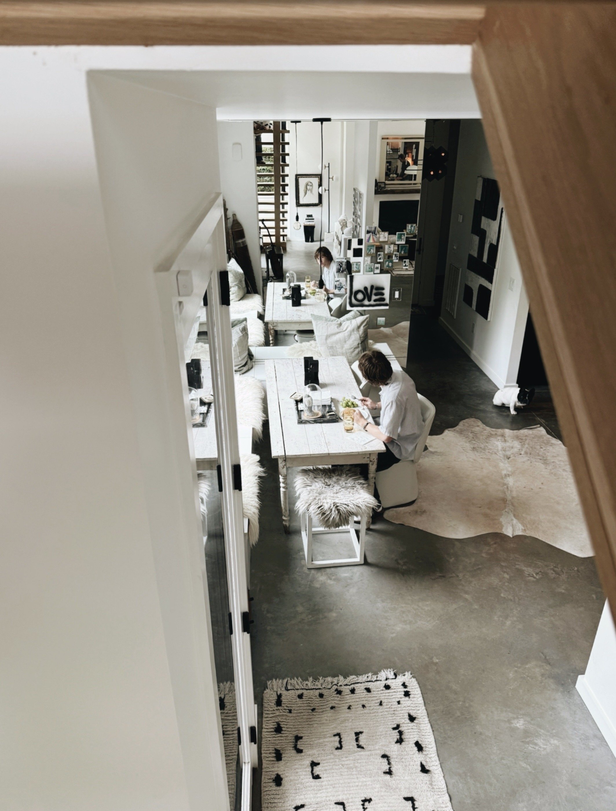View in the modern home of Michel Van Devender from an upstairs landing into a modern black and white home with artwork, collected objects, and a dining table below.