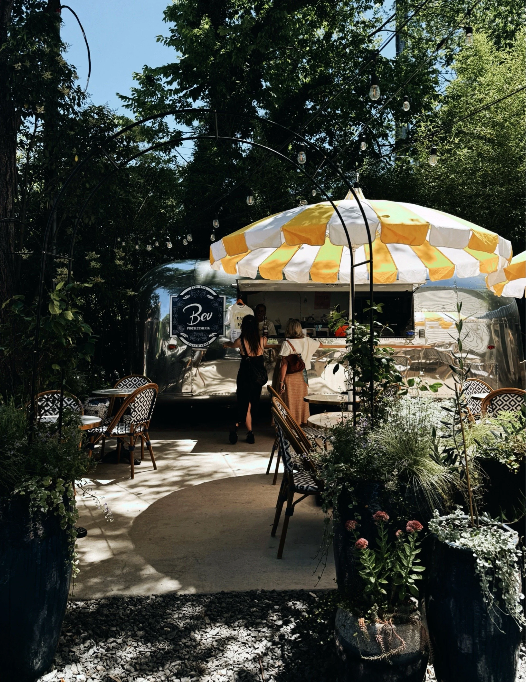 Vintage silver Airstream trailer converted into a Charlotte NC prosecco bar, Bev Proseccheria, with outdoor seating and greenery.