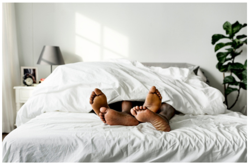 Couples in bed under blanket intimate with feet out.