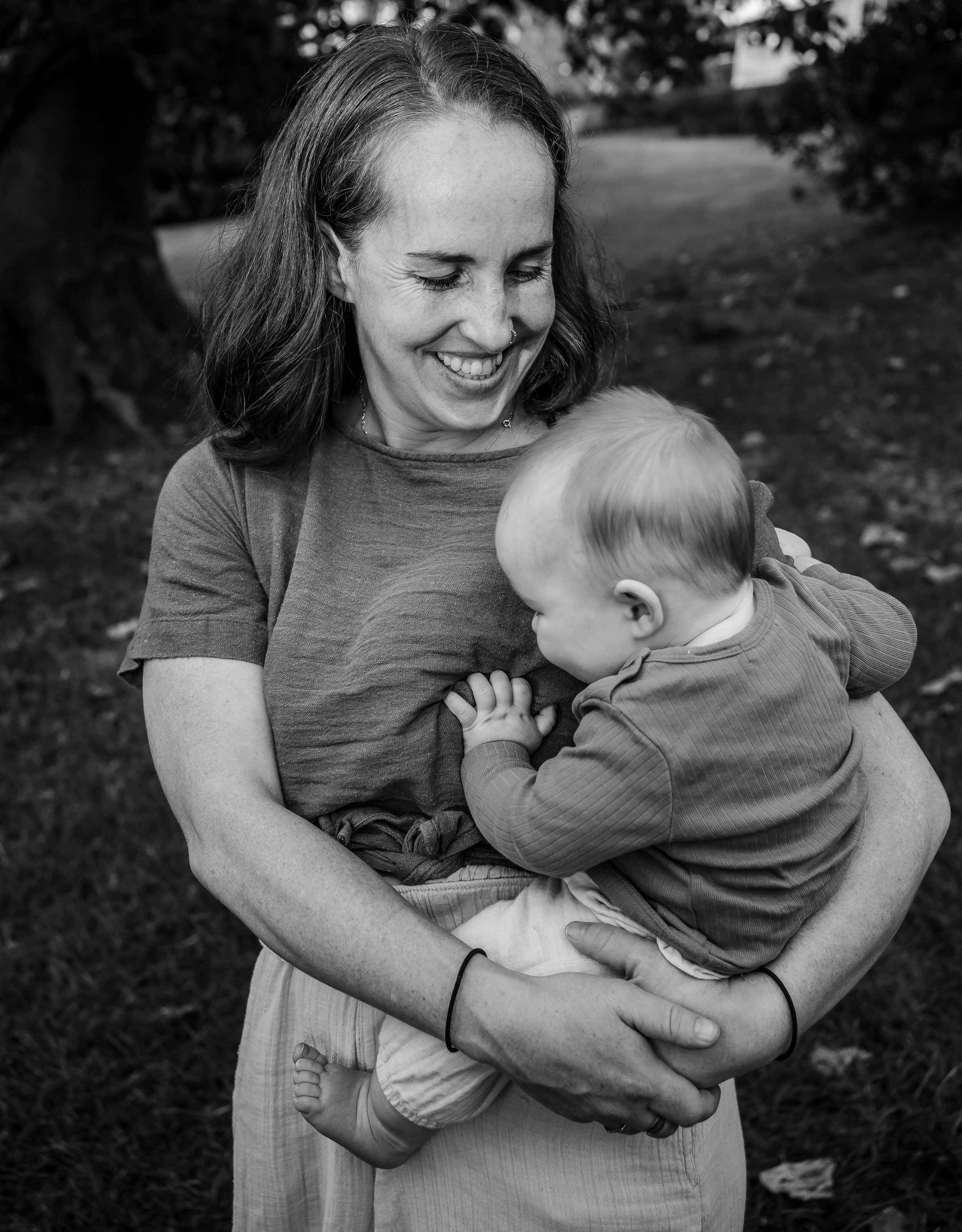 A mum holding a toddler outdoors, both smiling and sharing a moment.