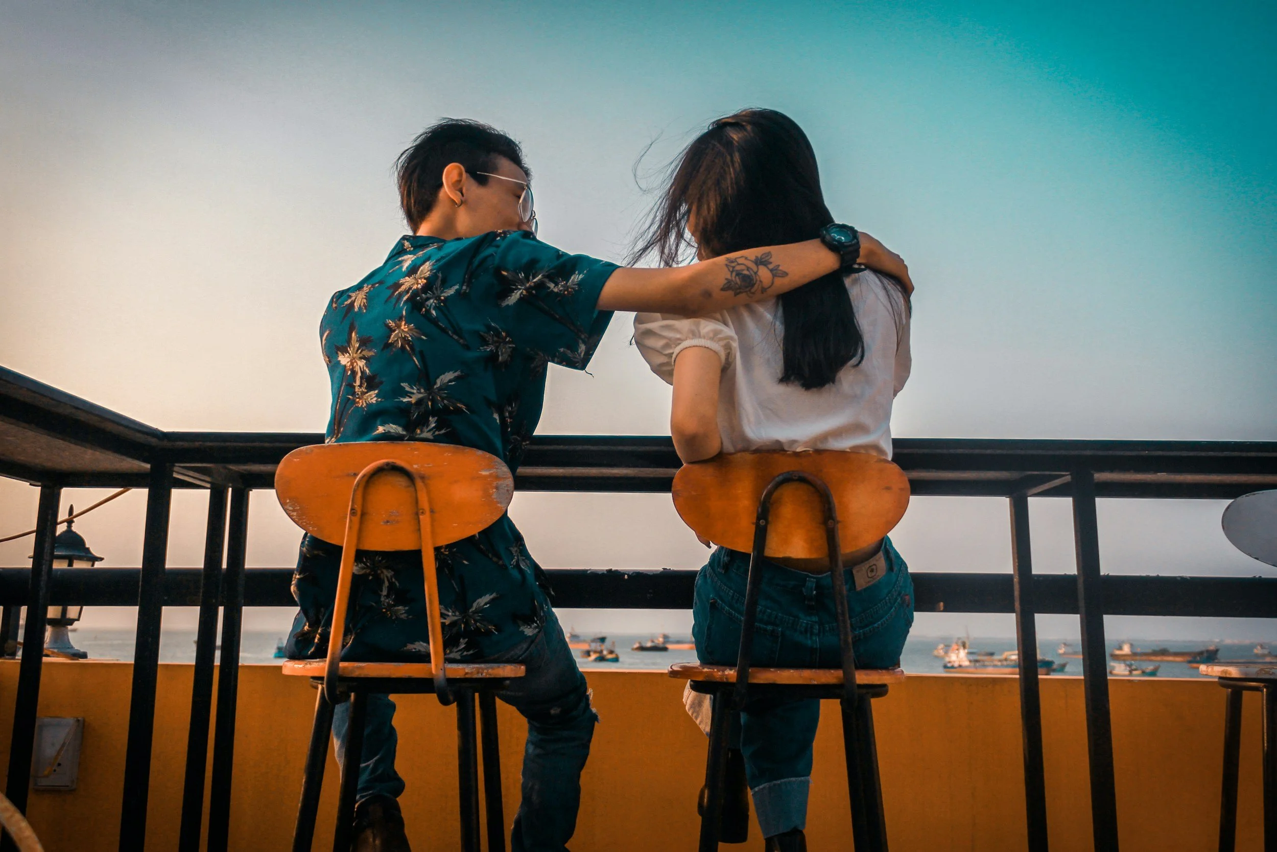 Couple sitting at a rooftop bar with an arm around each other, looking out over the water at sunset