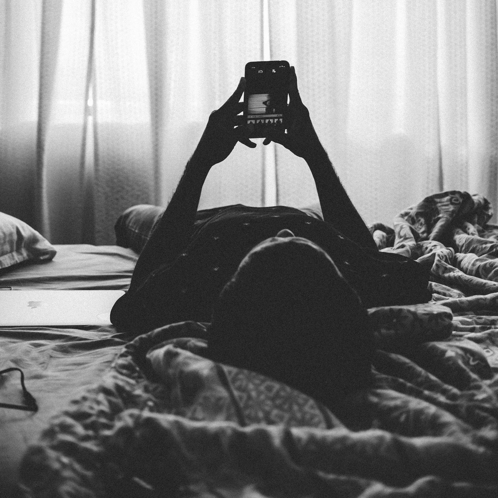 black and white photo of someone laying on their bed while holding their phone editing photos