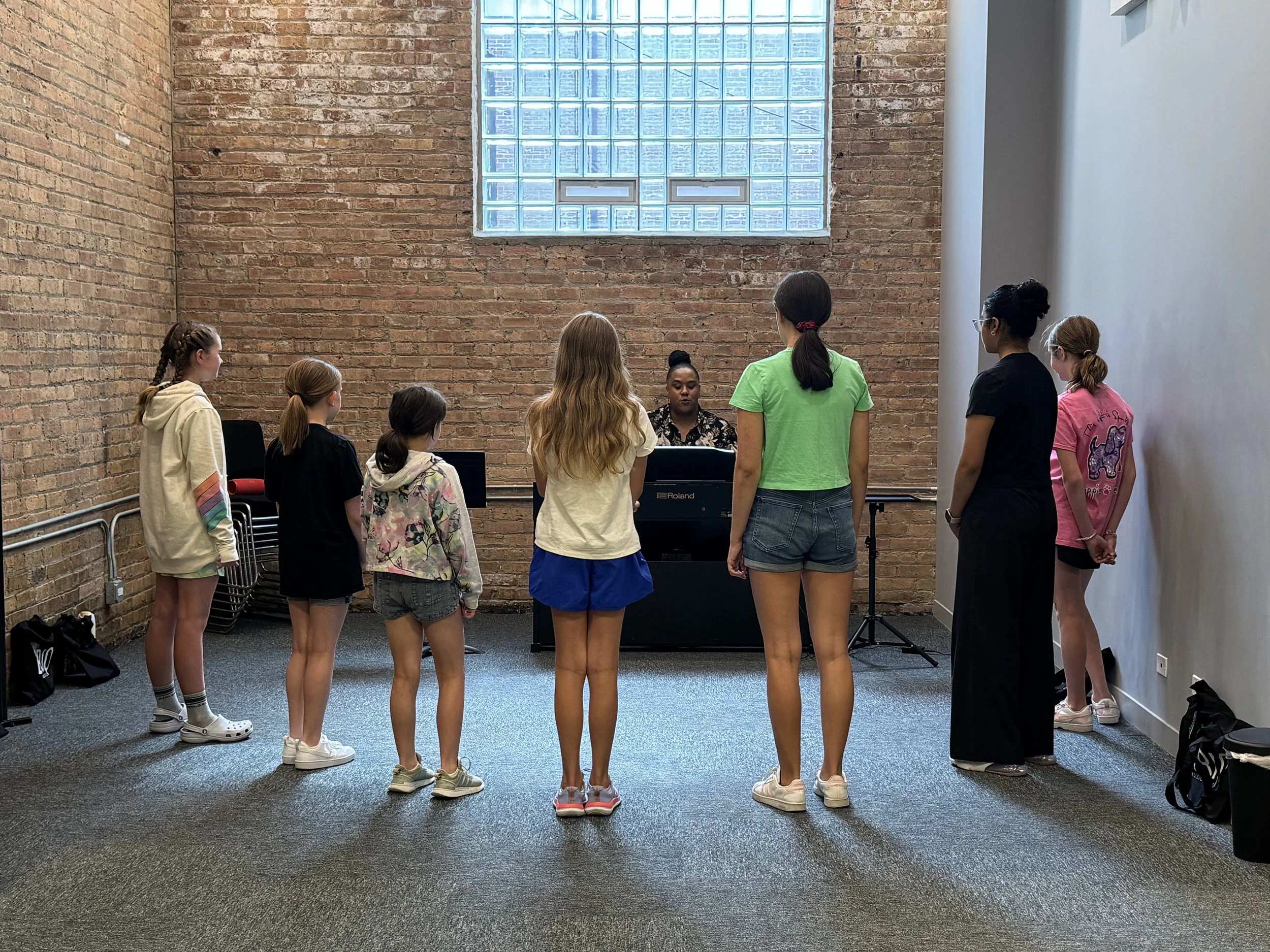Campers stand facing teacher during vocal rehearsal