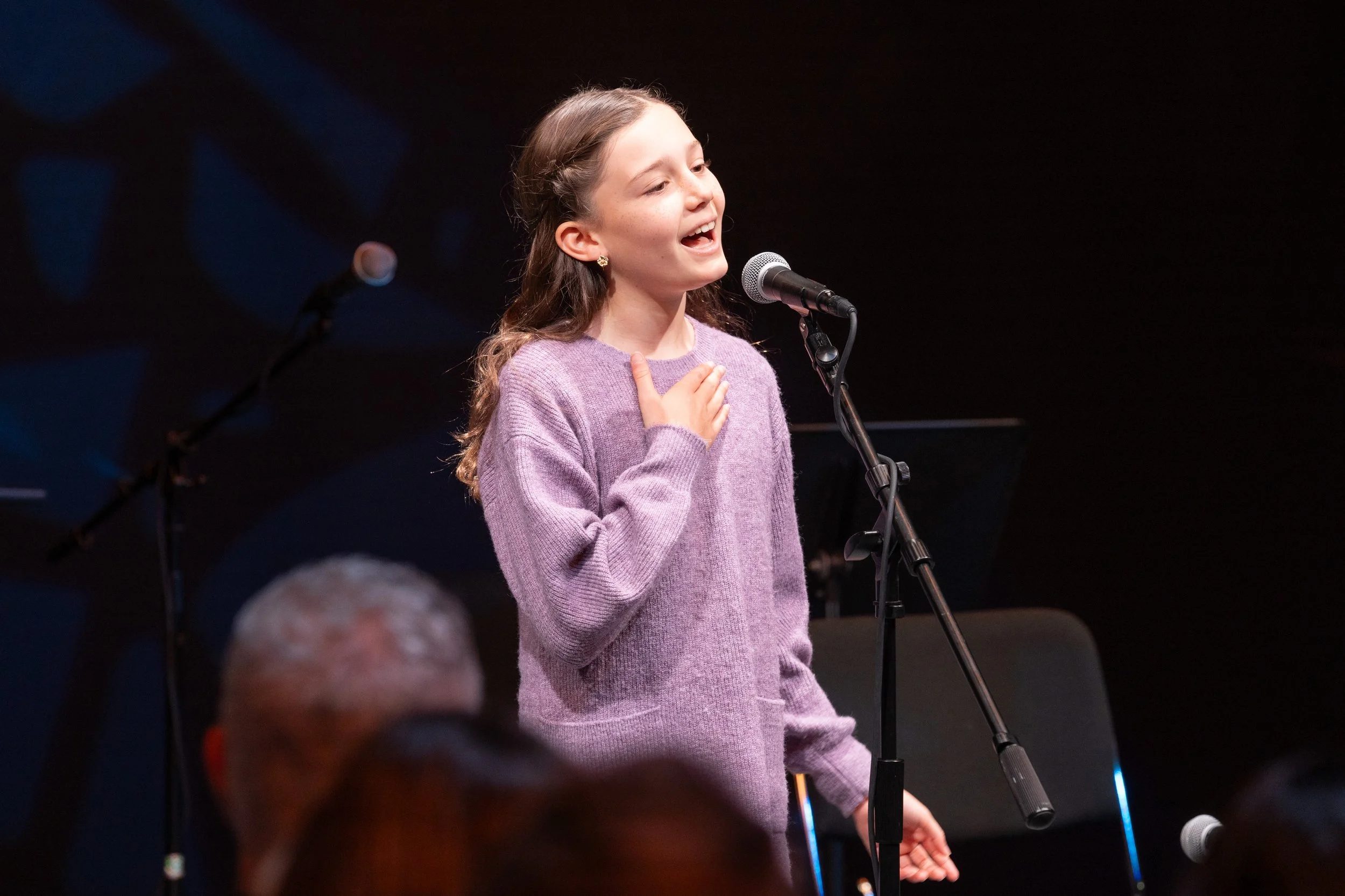 Pre-teen in purple sweater, singing into mircophone during performance
