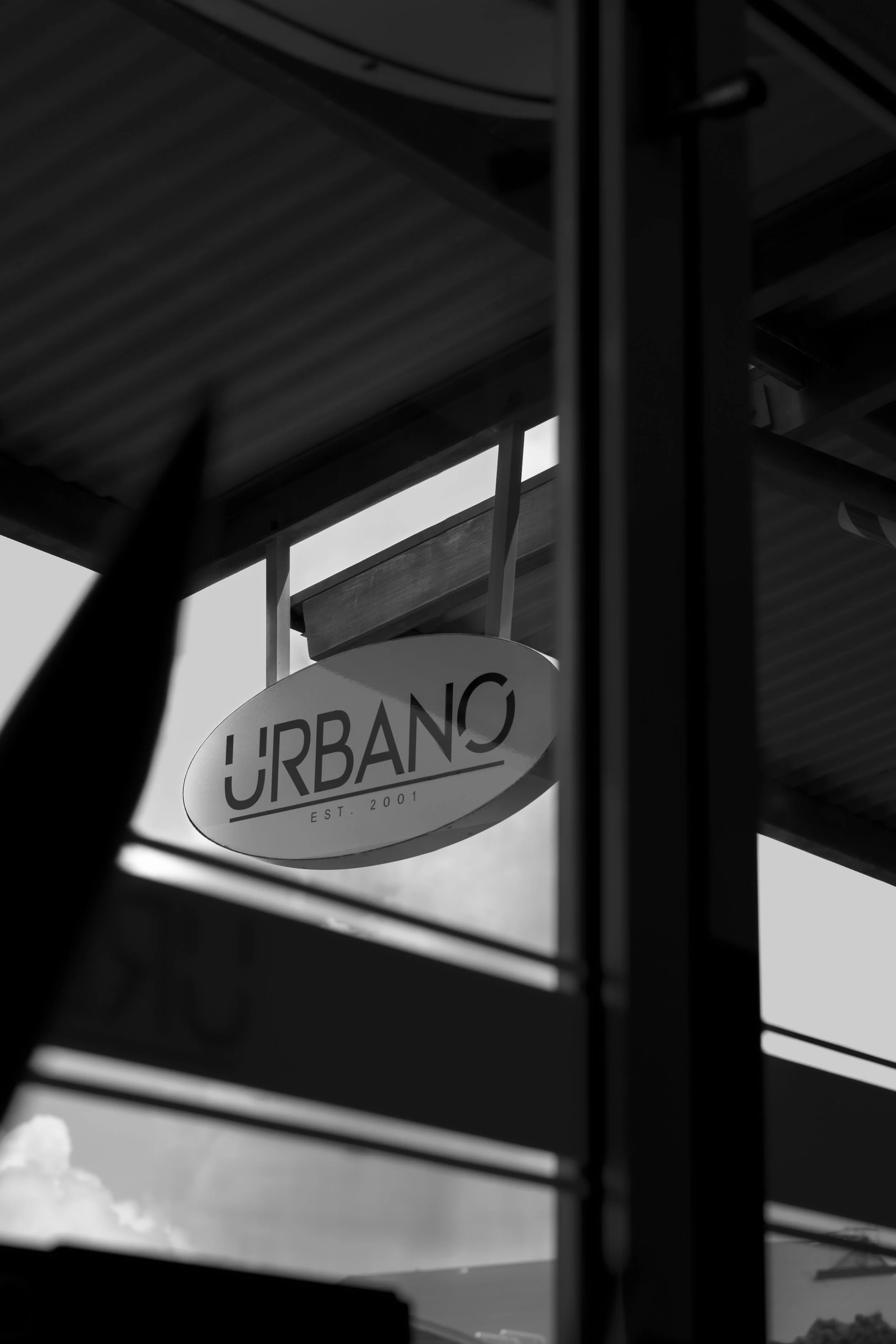 A low-moody photograph of the URBANO logo on the outdoor signage, taken from inside the barbershop