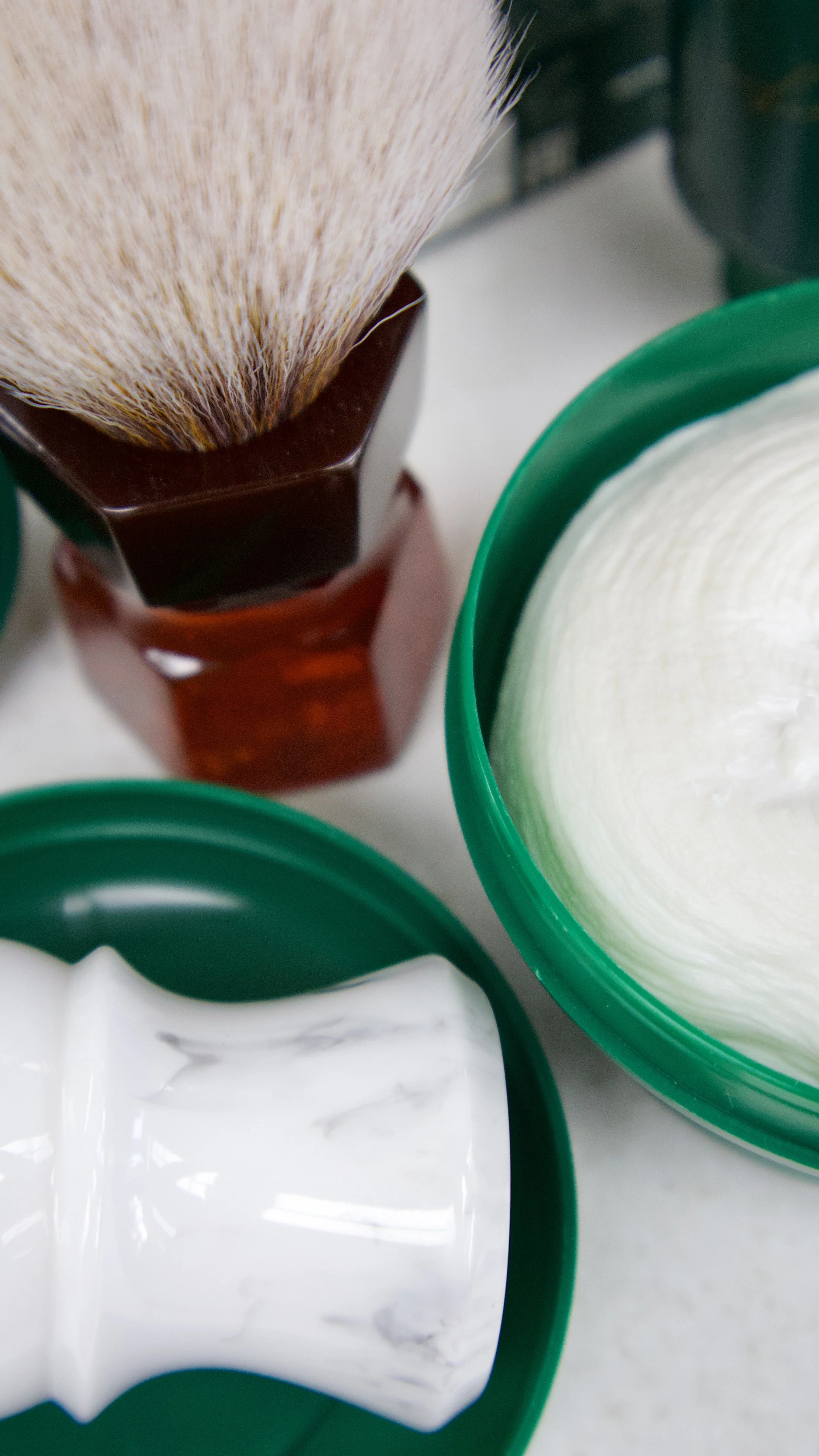 Close-up of various open containers with household products including a wooden brush, a white cream or lotion, and a bar of soap, on a white surface.