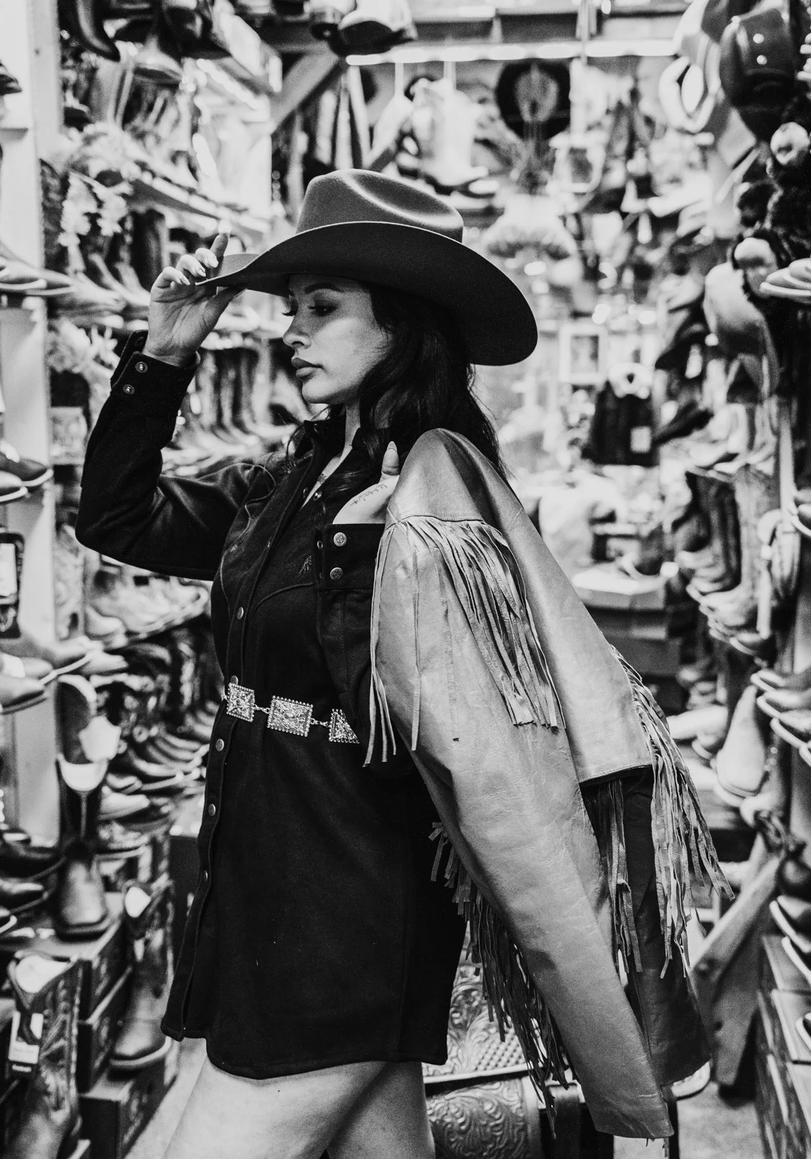 A woman in a cowboy hat and fringed jacket shopping for hats in a store